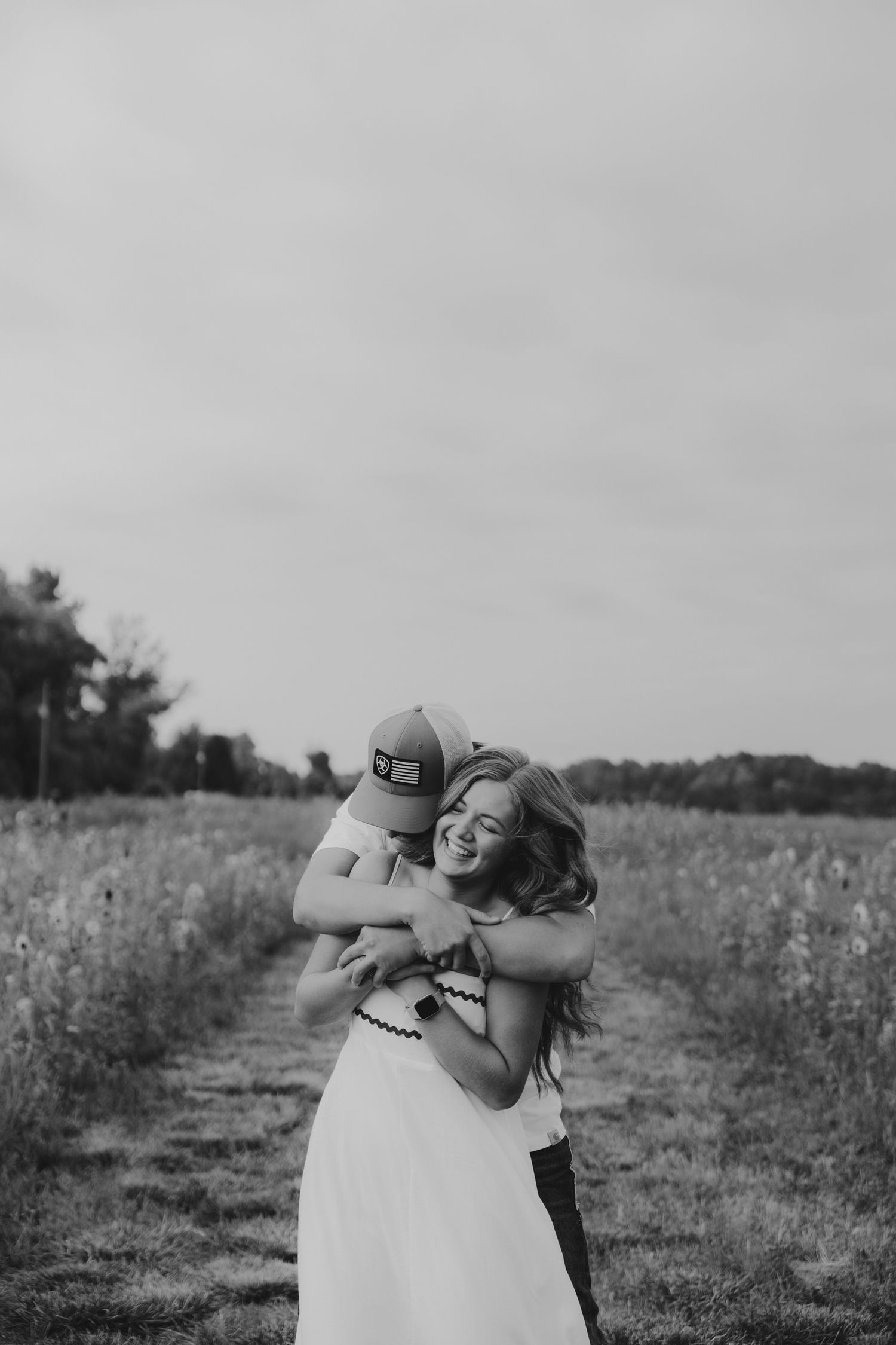 A couple embraces in a monochrome photo taken in a rustic outdoor setting.