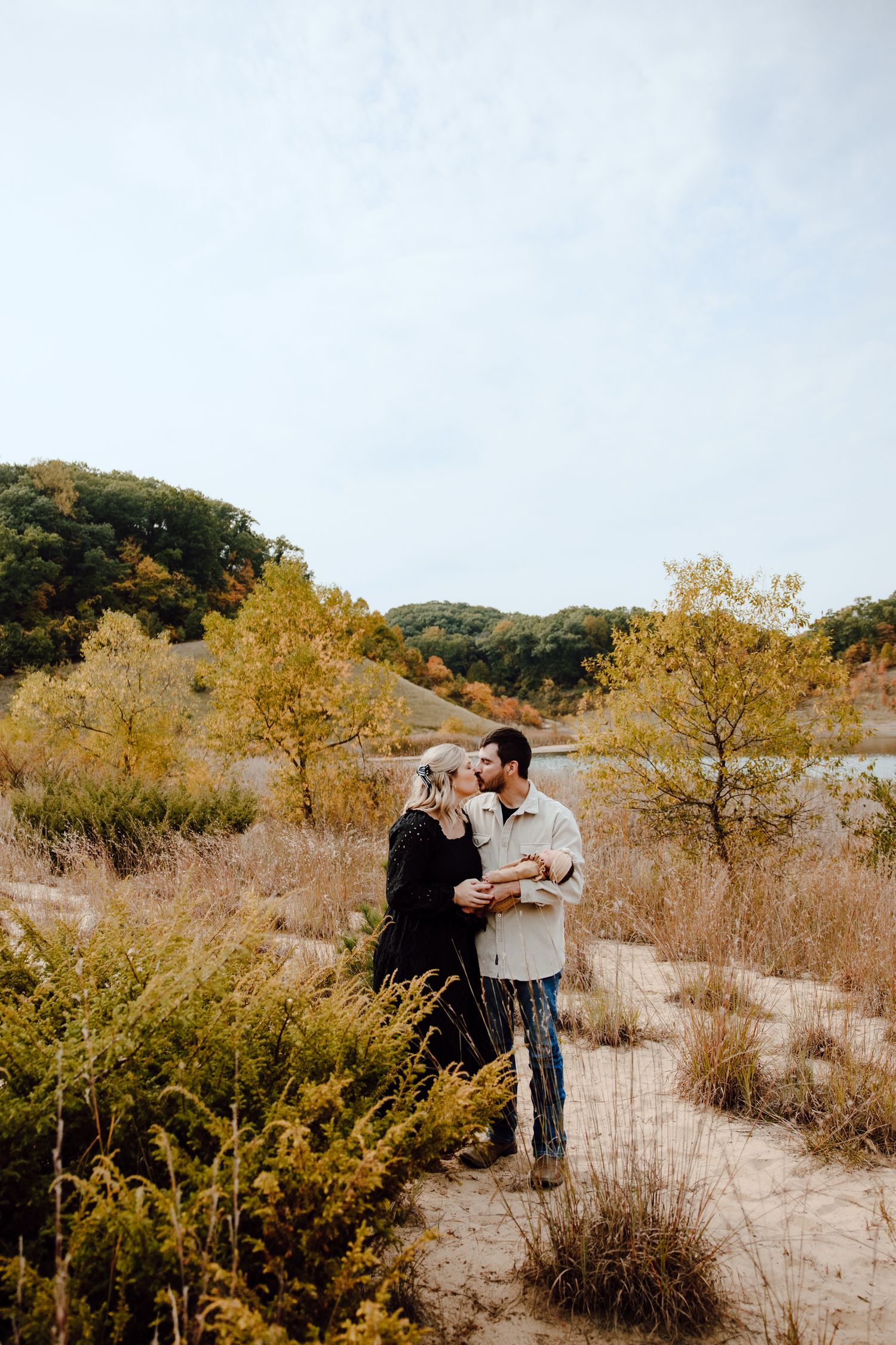 A couple shares an intimate moment among autumn foliage in a natural setting.