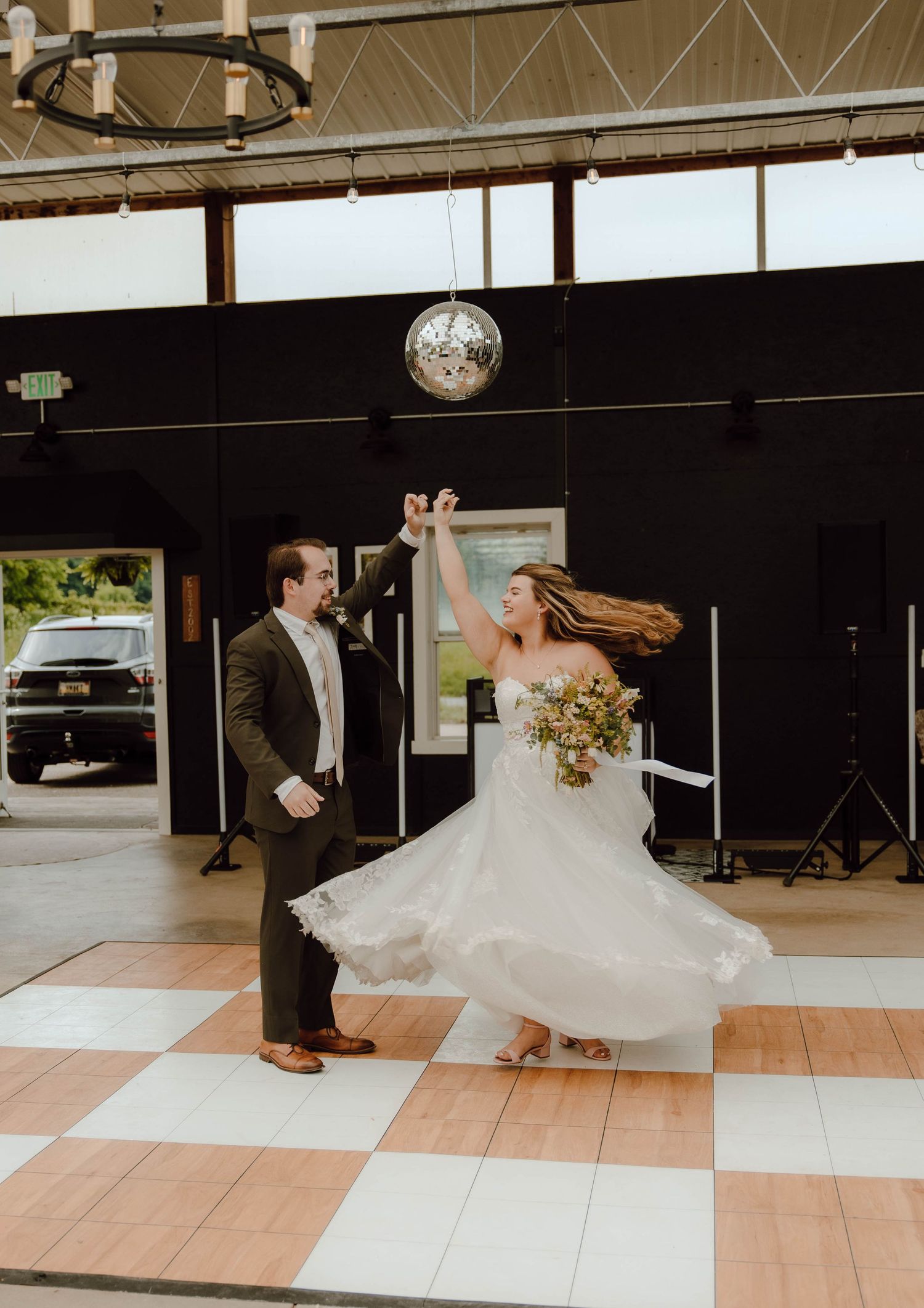 Bride and groom sharing first dance spin under disco ball on checkered dance floor at reception.