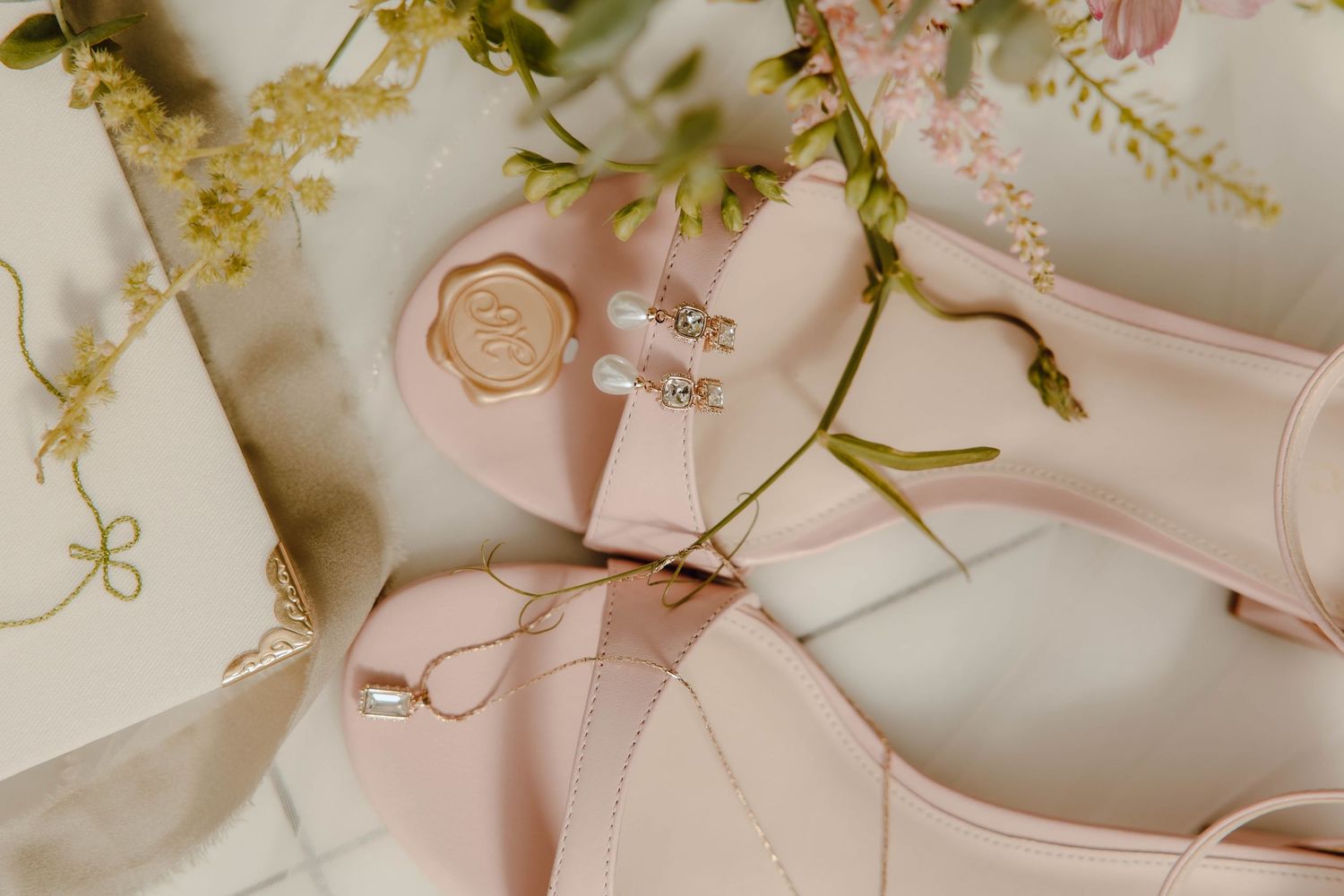Elegant blush pink bridal heels with gold wax seal and floral accents on marble surface.