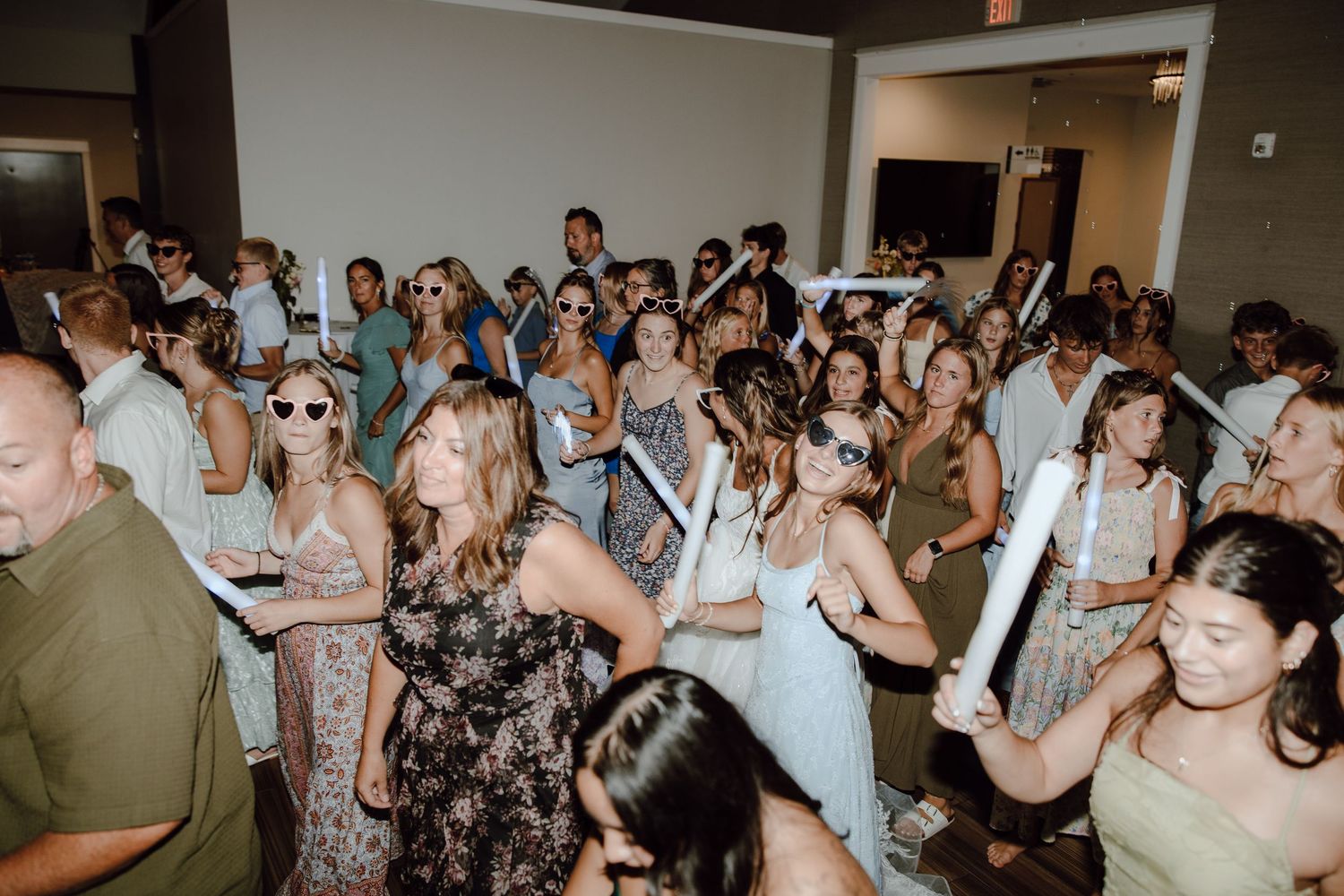Guests dancing and celebrating at lively indoor wedding reception party with glow sticks.