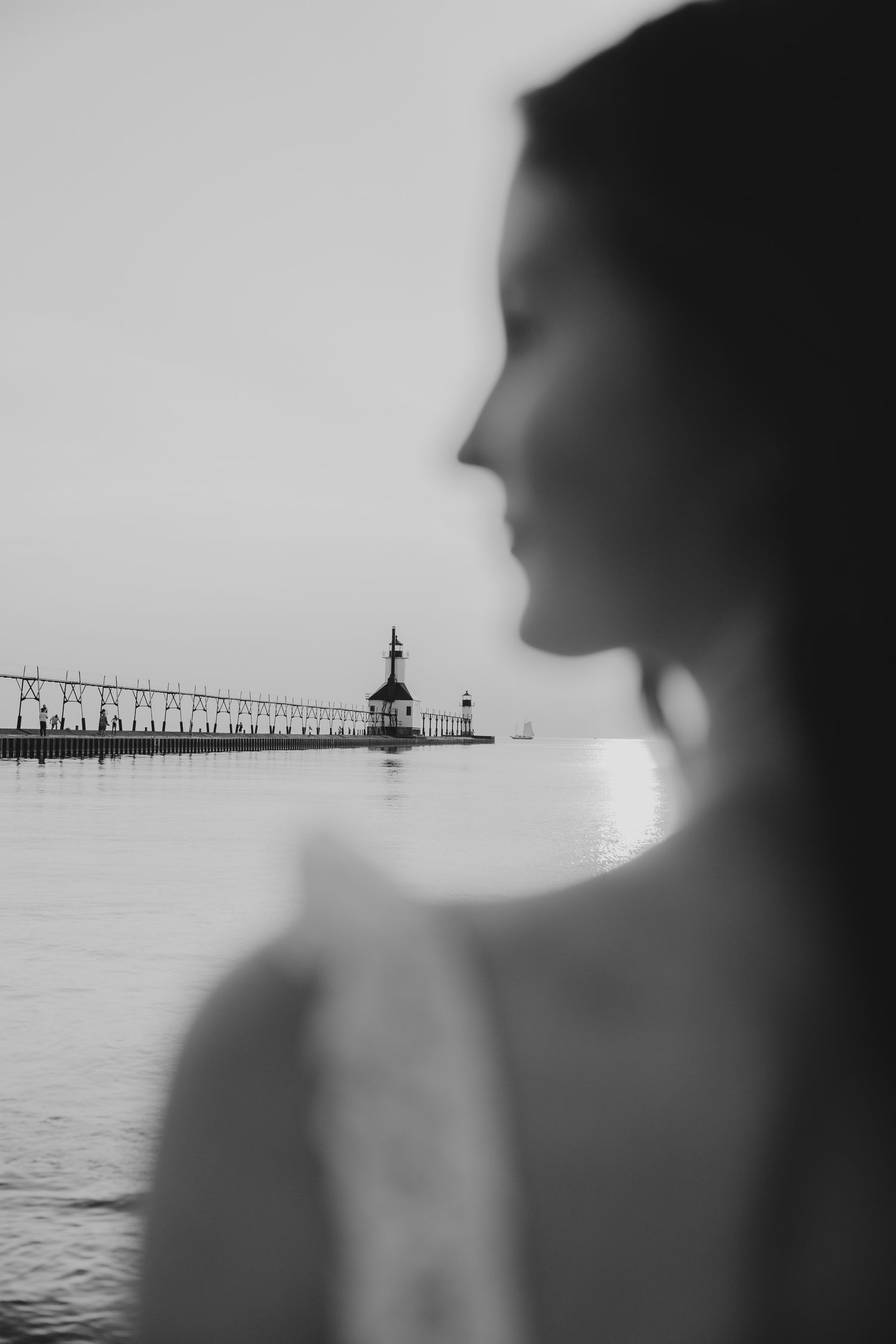 Silhouetted view of a lighthouse pier over calm waters in black and white.