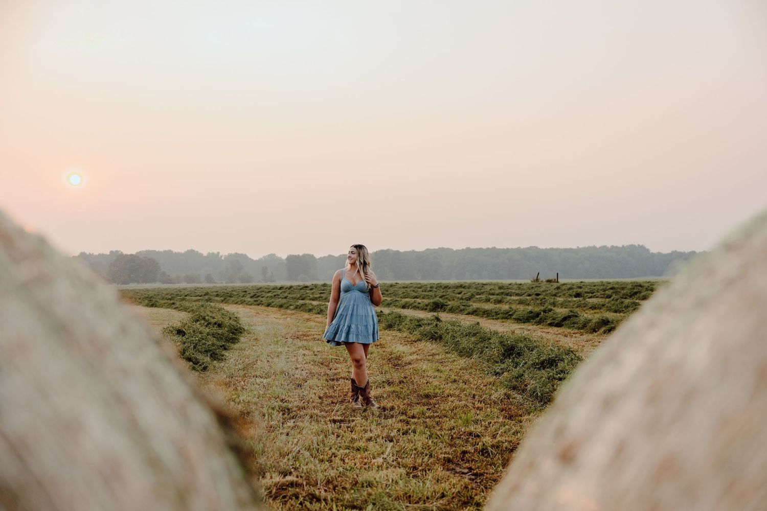 A pastoral landscape view of farmland at sunset with hay bales in the distance.