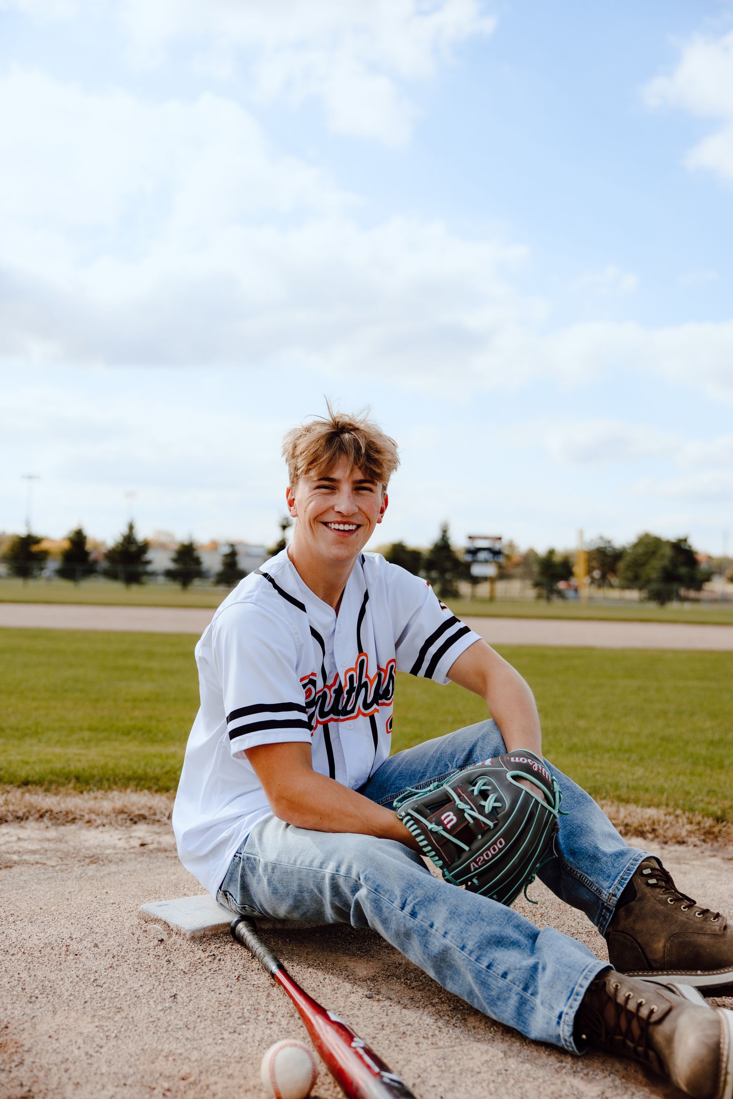 Baseball player in Panthers jersey sitting on field with glove and equipment.