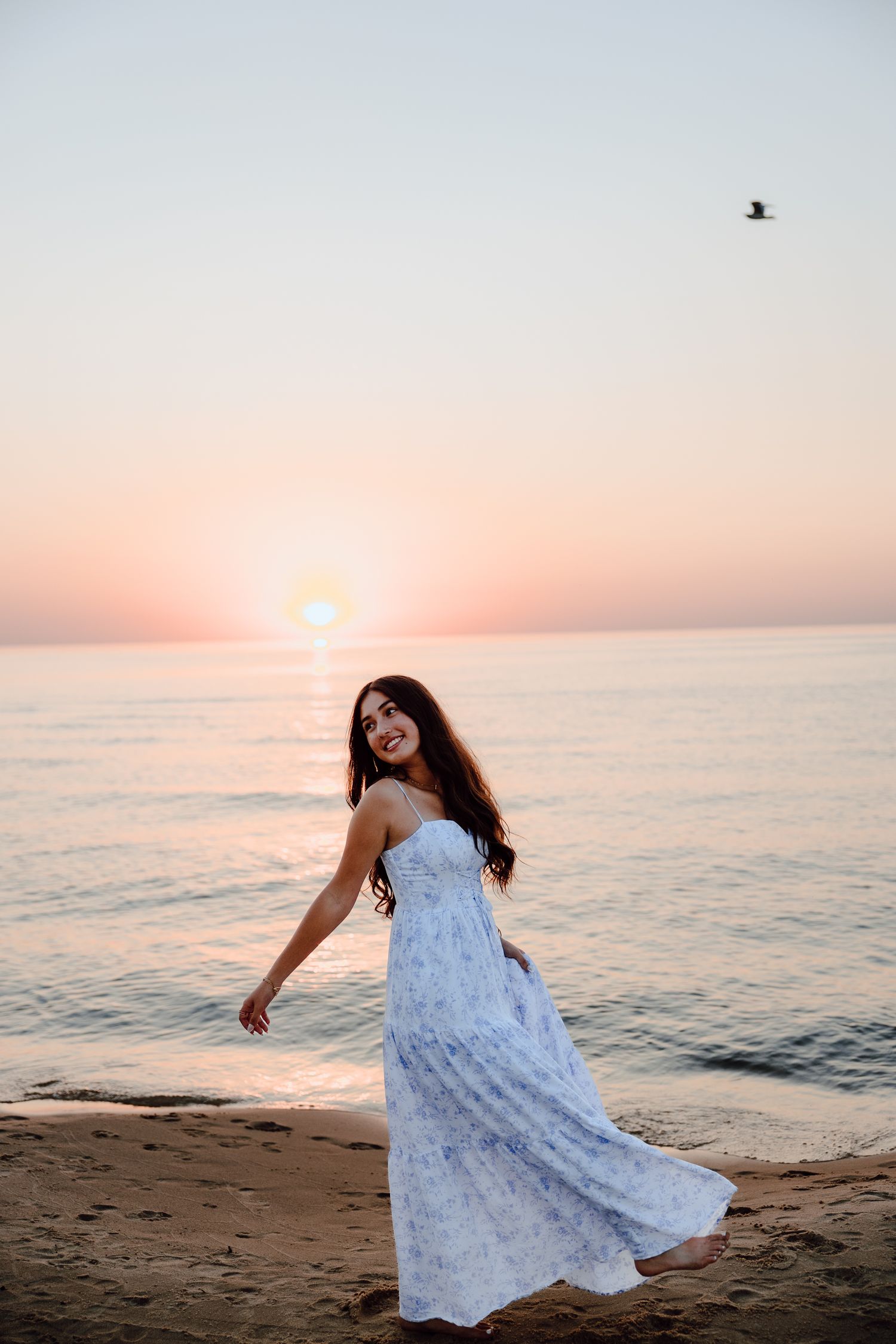 Dancing in a white dress on the beach as the sun sets over the horizon.