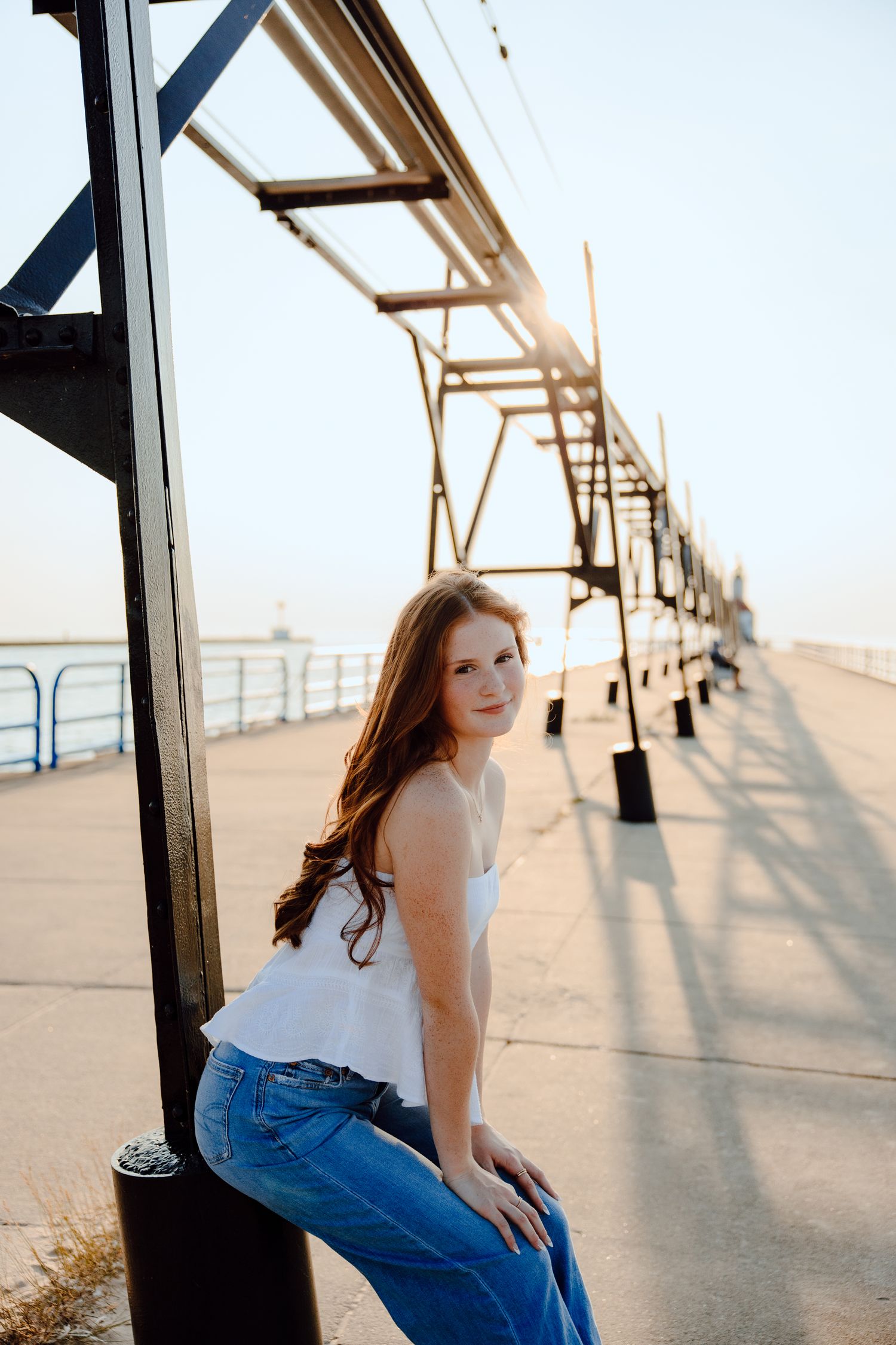 Someone in casual attire poses along a pier railing at sunset.