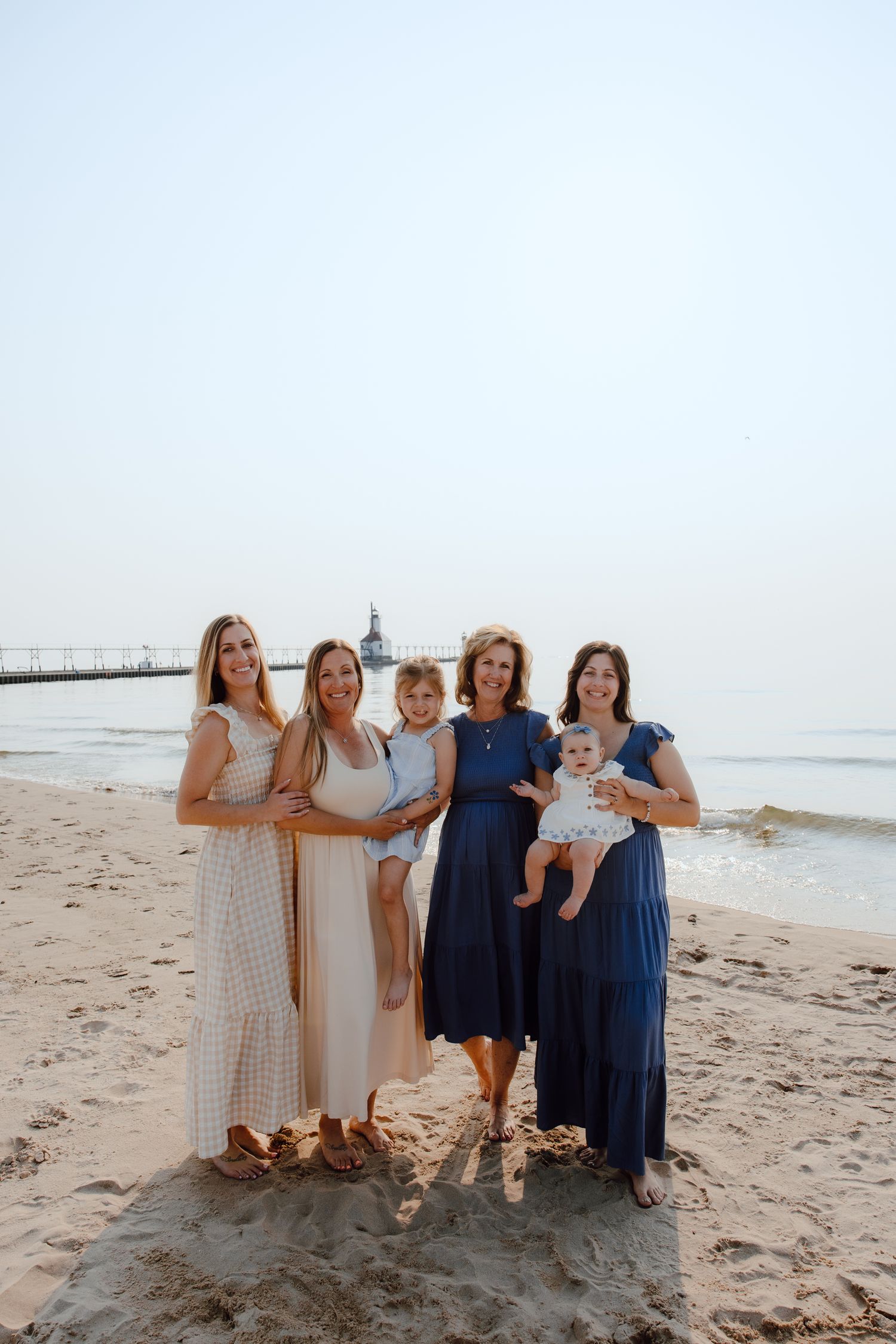 Group portrait of women and children in coordinating dresses on a beach.