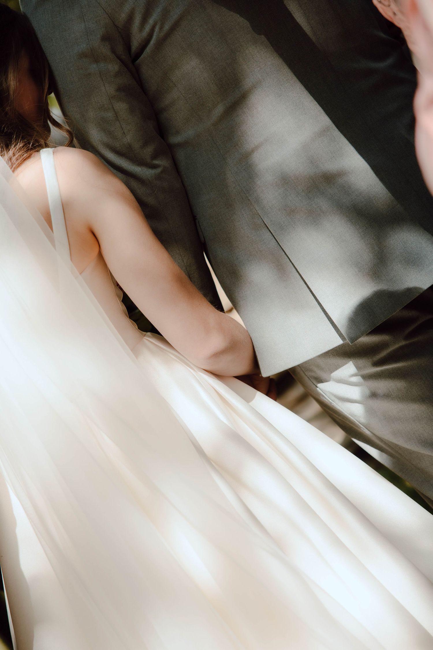 Artistic close-up of bride in white gown holding grooms hand in soft motion-blurred light during wedding.