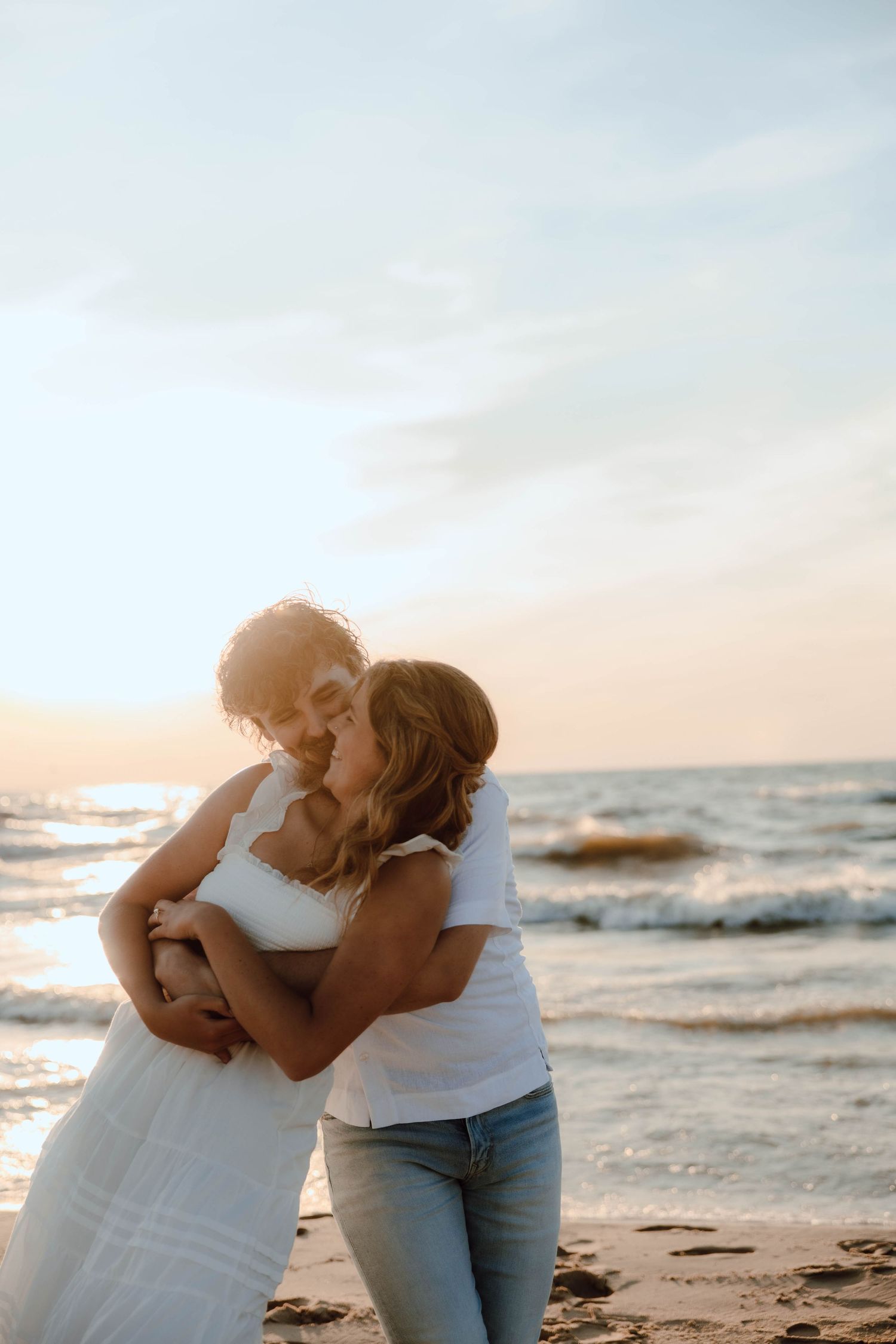 Couple embracing romantically on a sandy beach at sunset with ocean waves in the background.