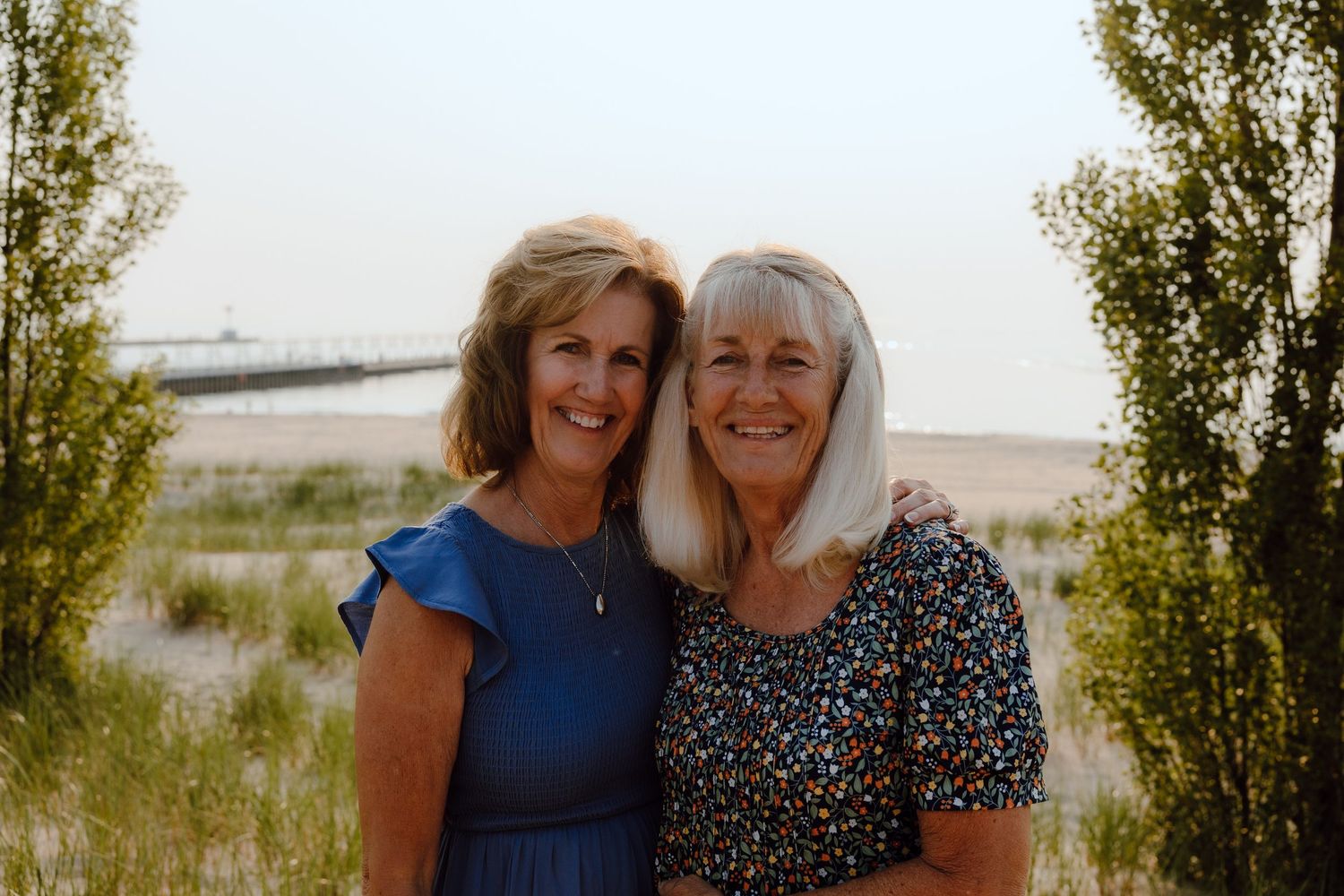 Two women in blue and patterned dresses pose together outdoors.