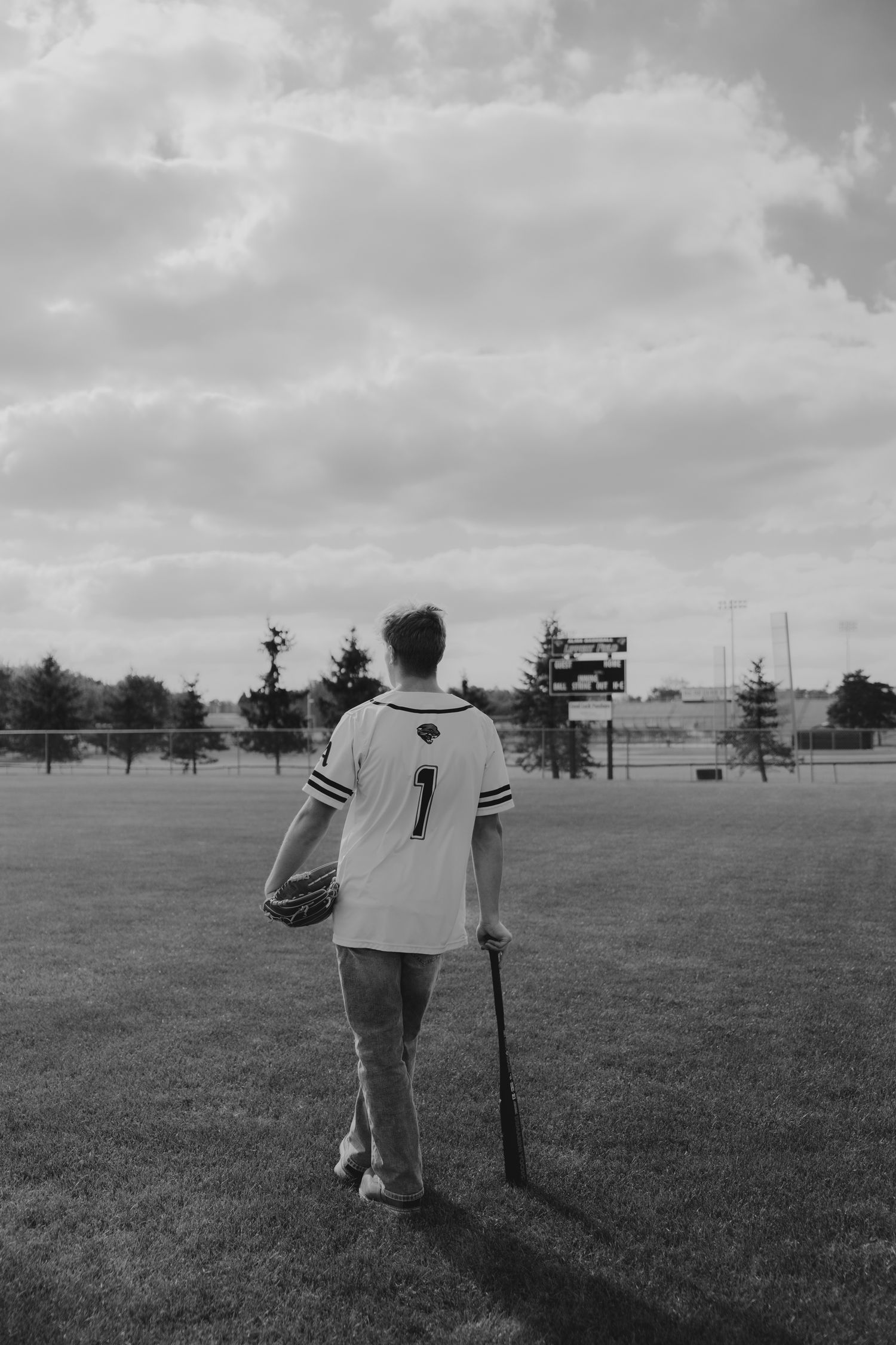 Black and white portrait of baseball player standing in empty field with bat.