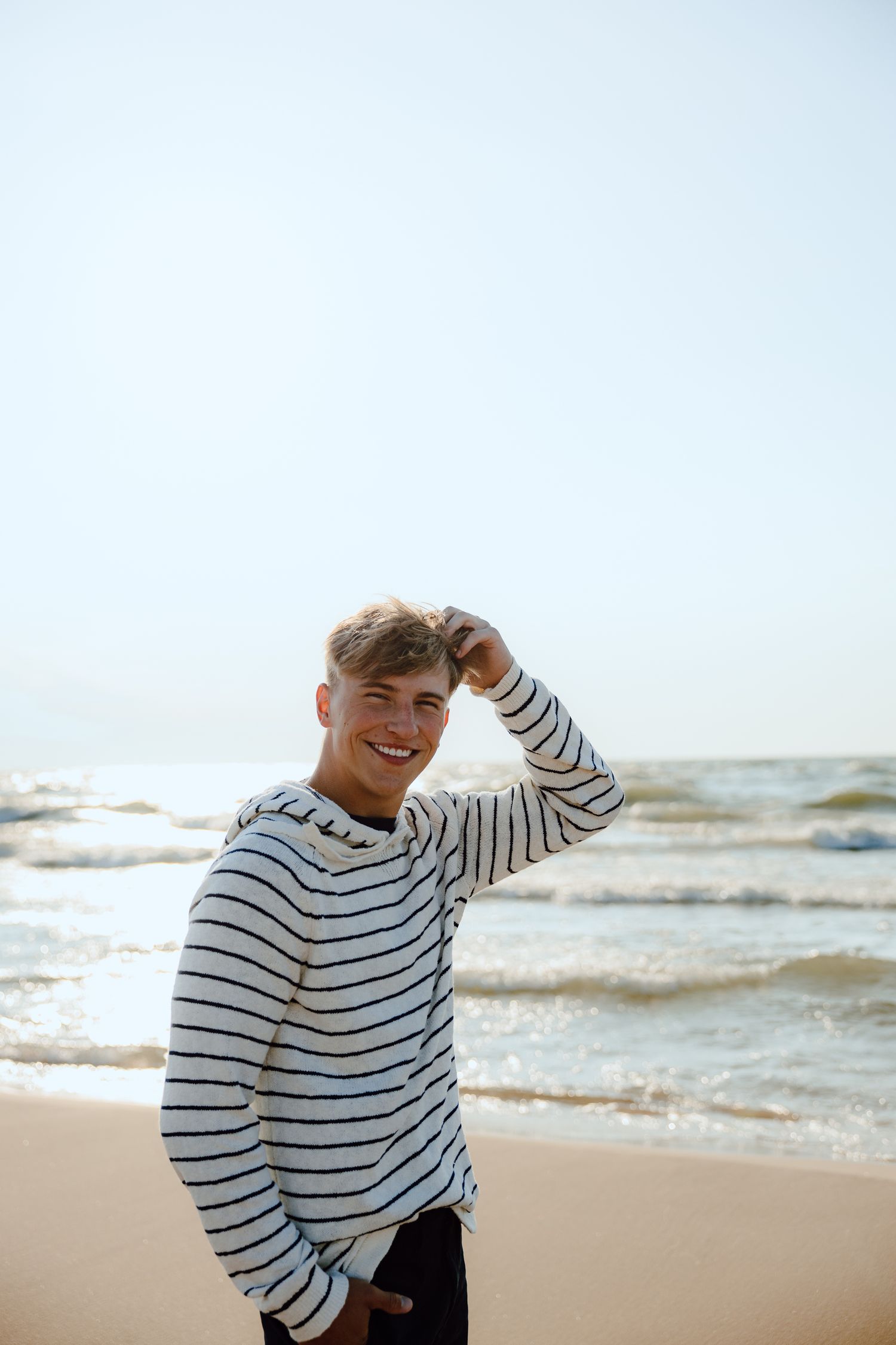 Person in striped sweater posing on beach with ocean waves in background.