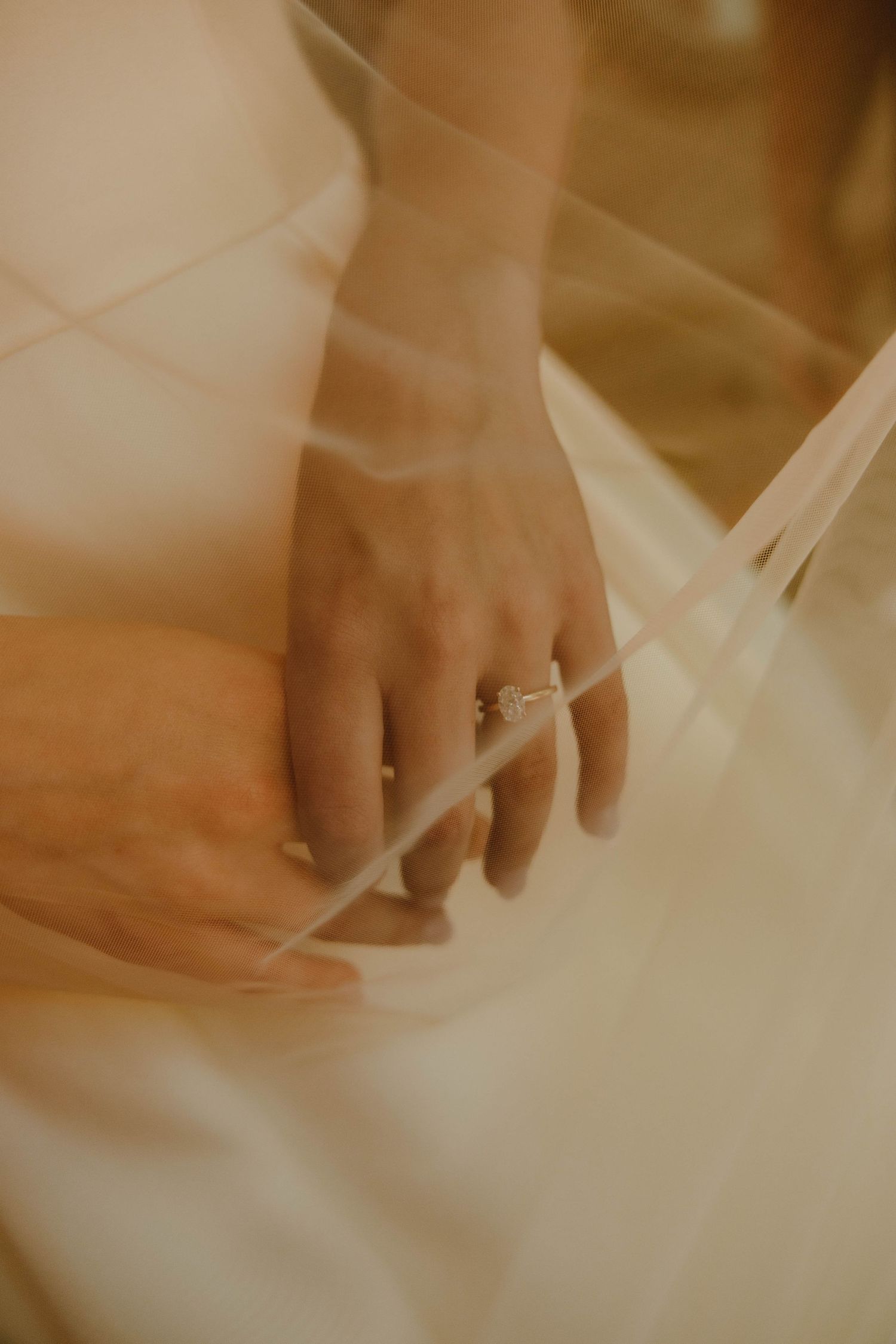 Close-up of a bride's hand adorned with a diamond engagement ring, draped under a sheer wedding veil.