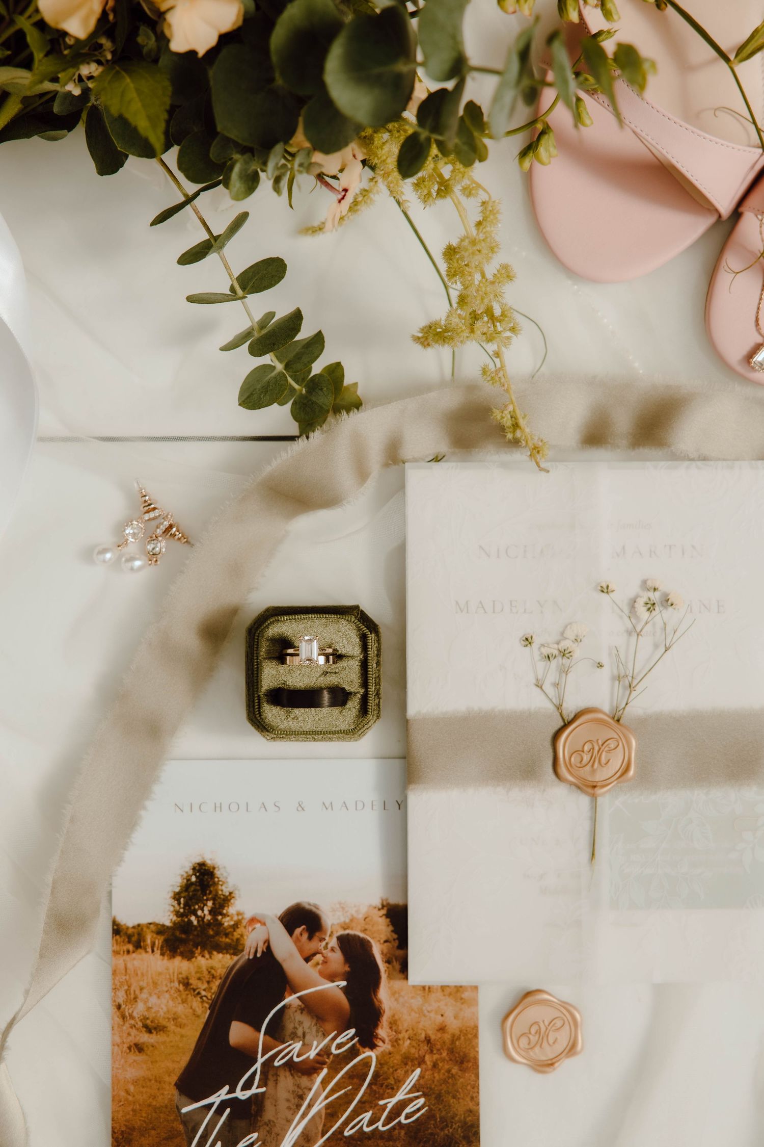 Wedding flat lay with rings, save the date card, floral bouquet, wax seal invitation, and blush heels.