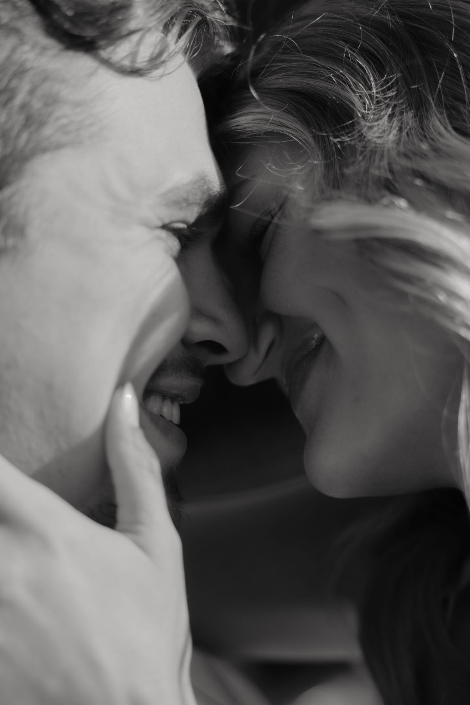 Black and white close-up of a romantic couple smiling and touching foreheads in an intimate moment.