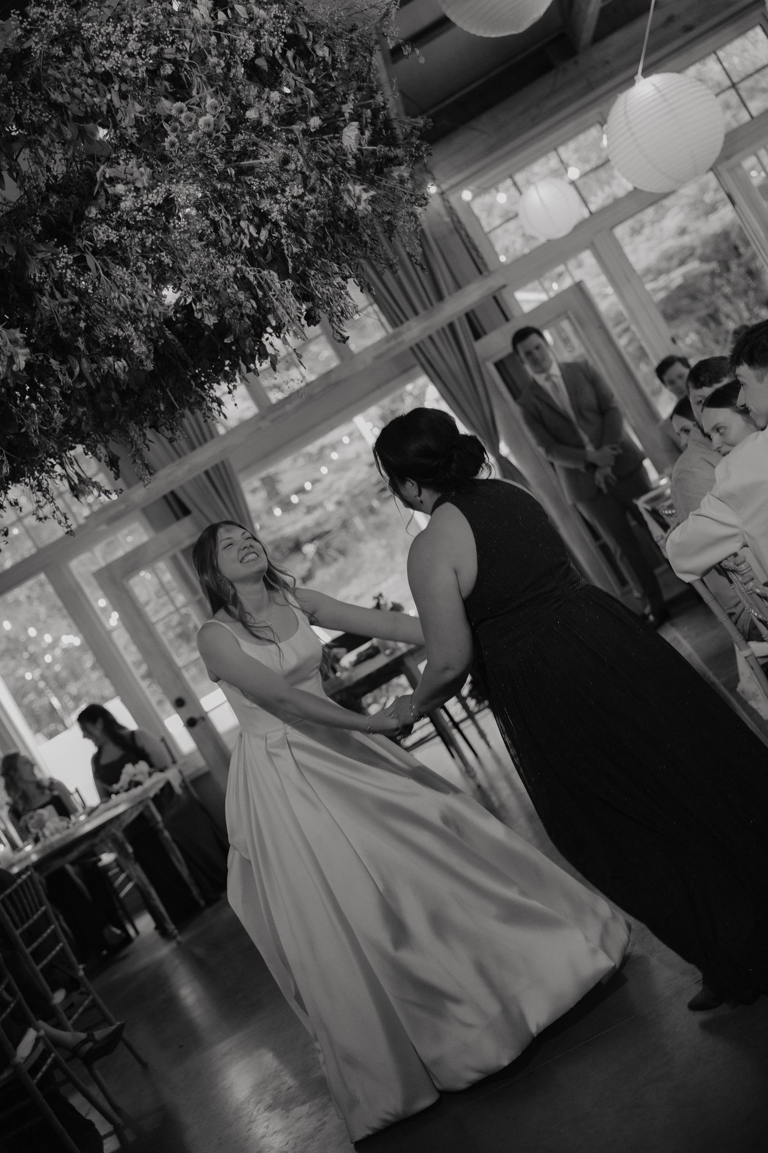 Black and white photo of bride sharing a tender dance moment with a guest at an indoor wedding reception.