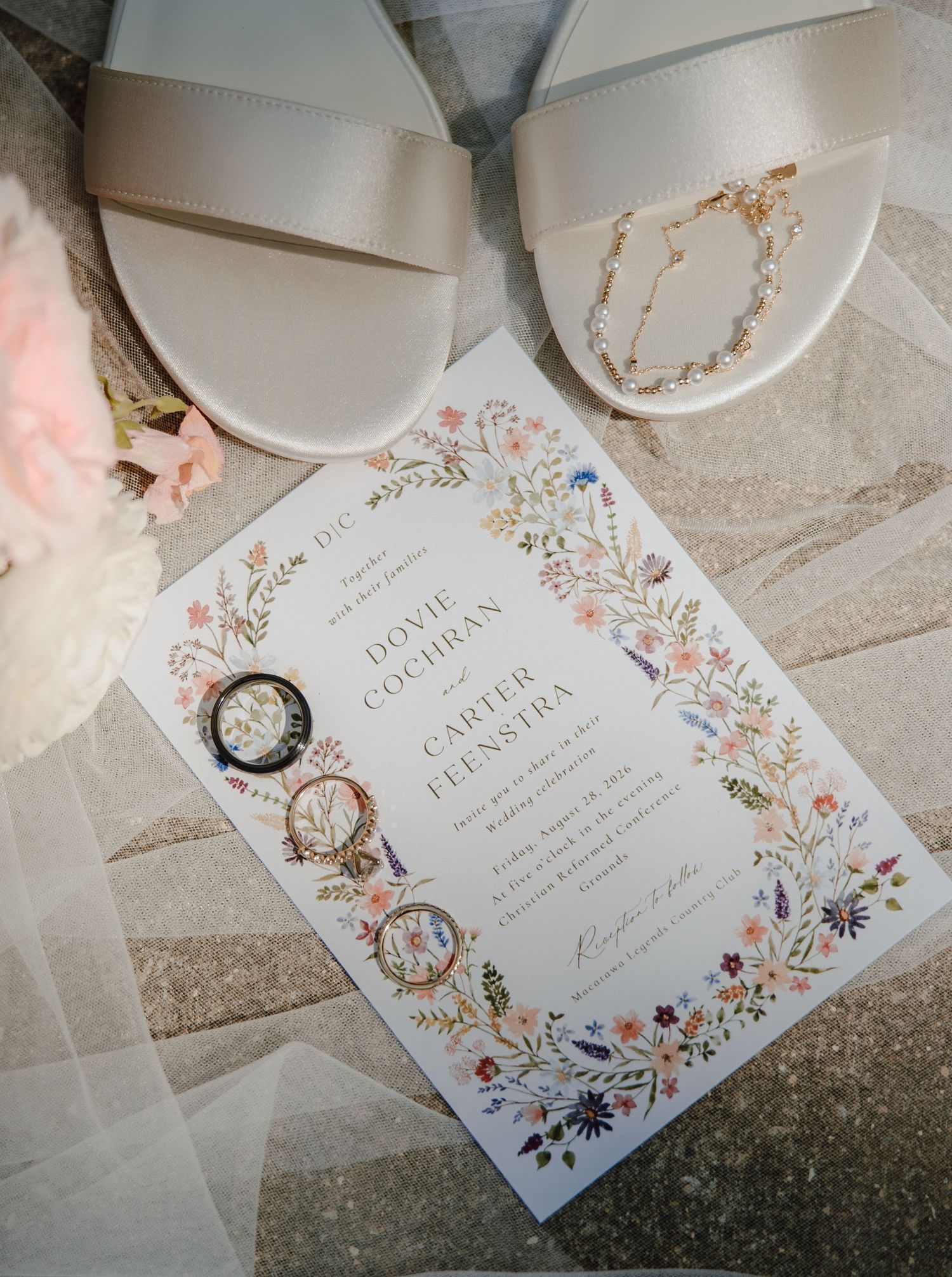 Elegant wedding flat lay with floral invitation, pearl shoes, gold rings, and anklet on marble.