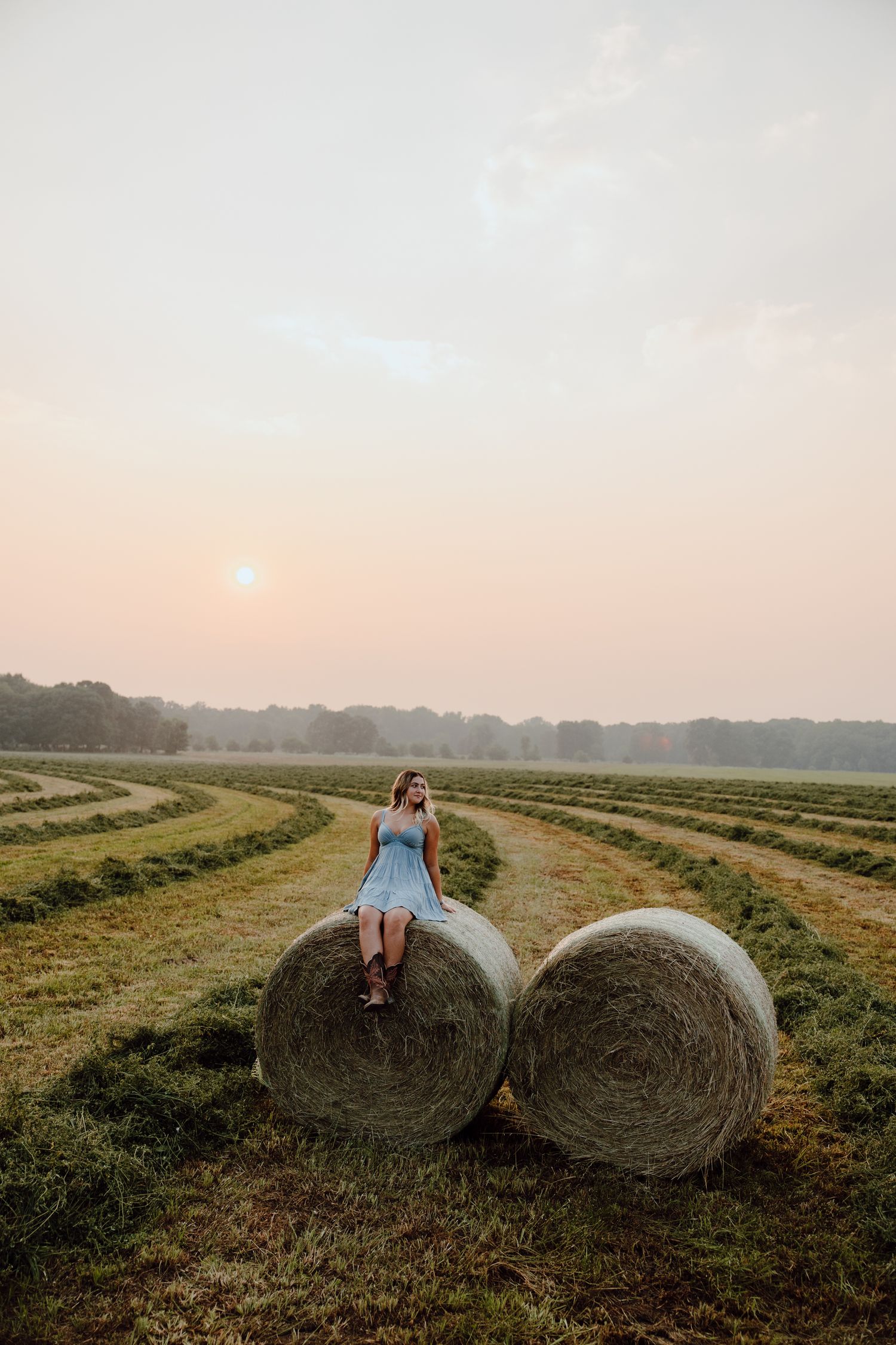 Large round hay bales sit in a harvested field during golden hour.