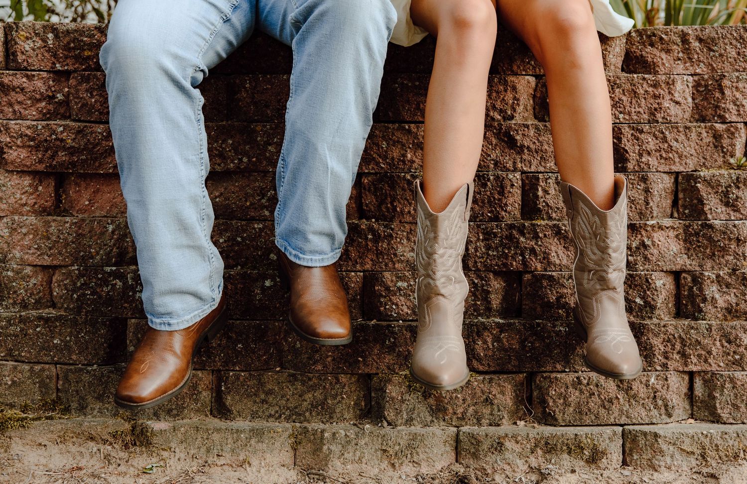 Two pairs of legs dangling from a brick wall showing boots and jeans.