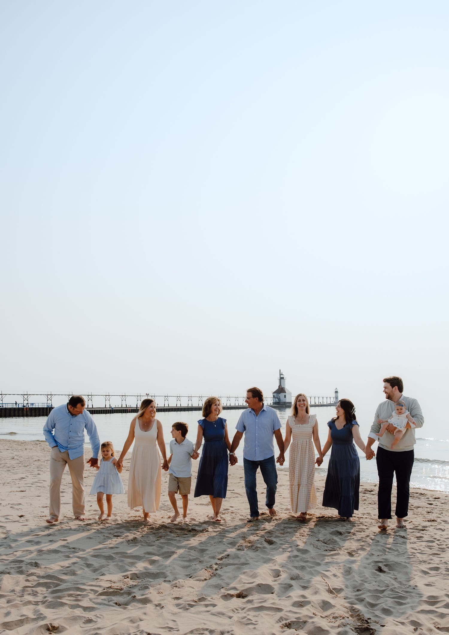Family walking together on a sandy beach with a pier visible in the distance.