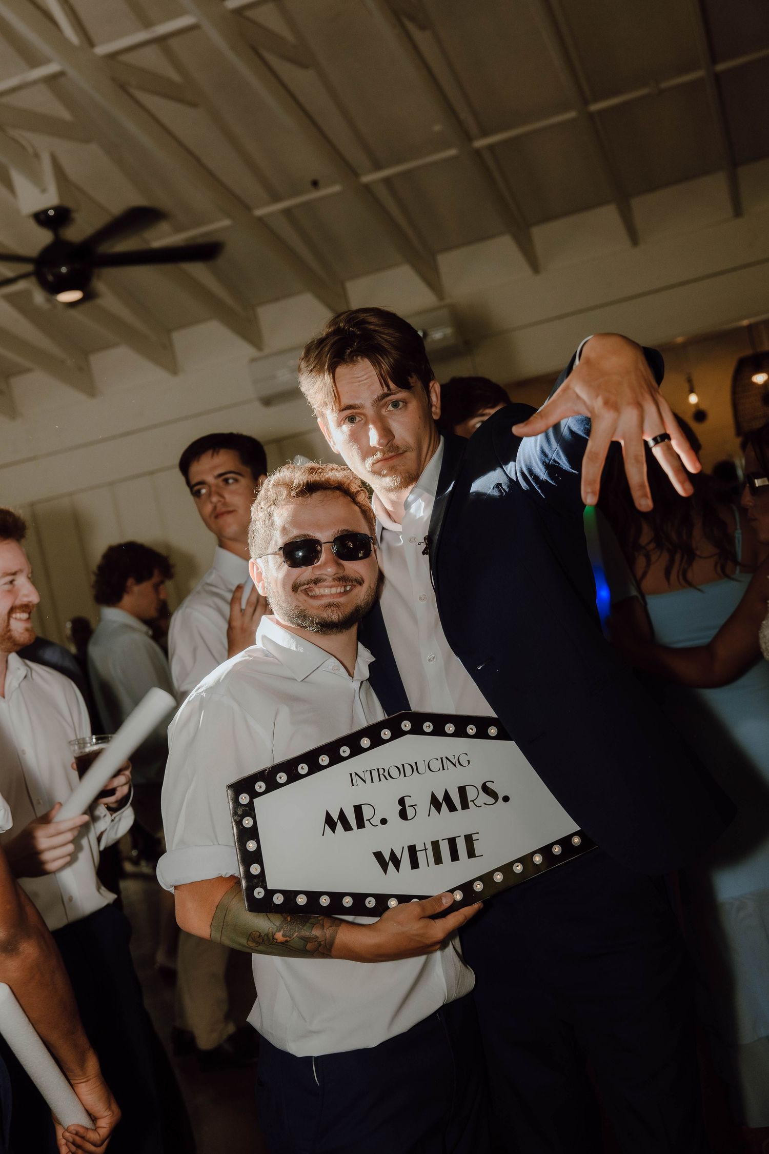 Wedding guests celebrating at reception holding Mr. & Mrs. White marquee sign while posing and dancing together.