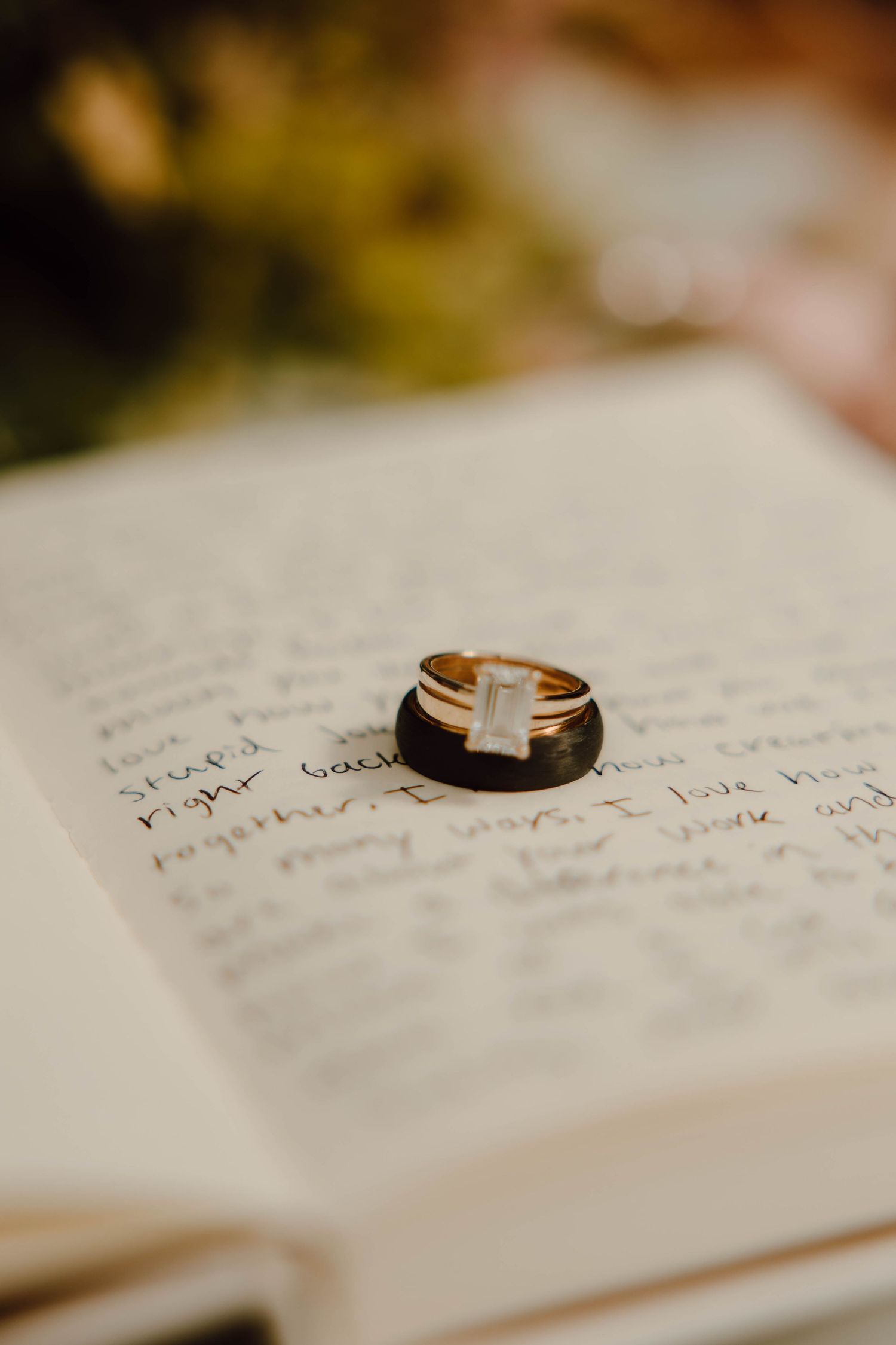 Gold wedding rings with a baguette diamond sit atop an open journal with handwritten vows.
