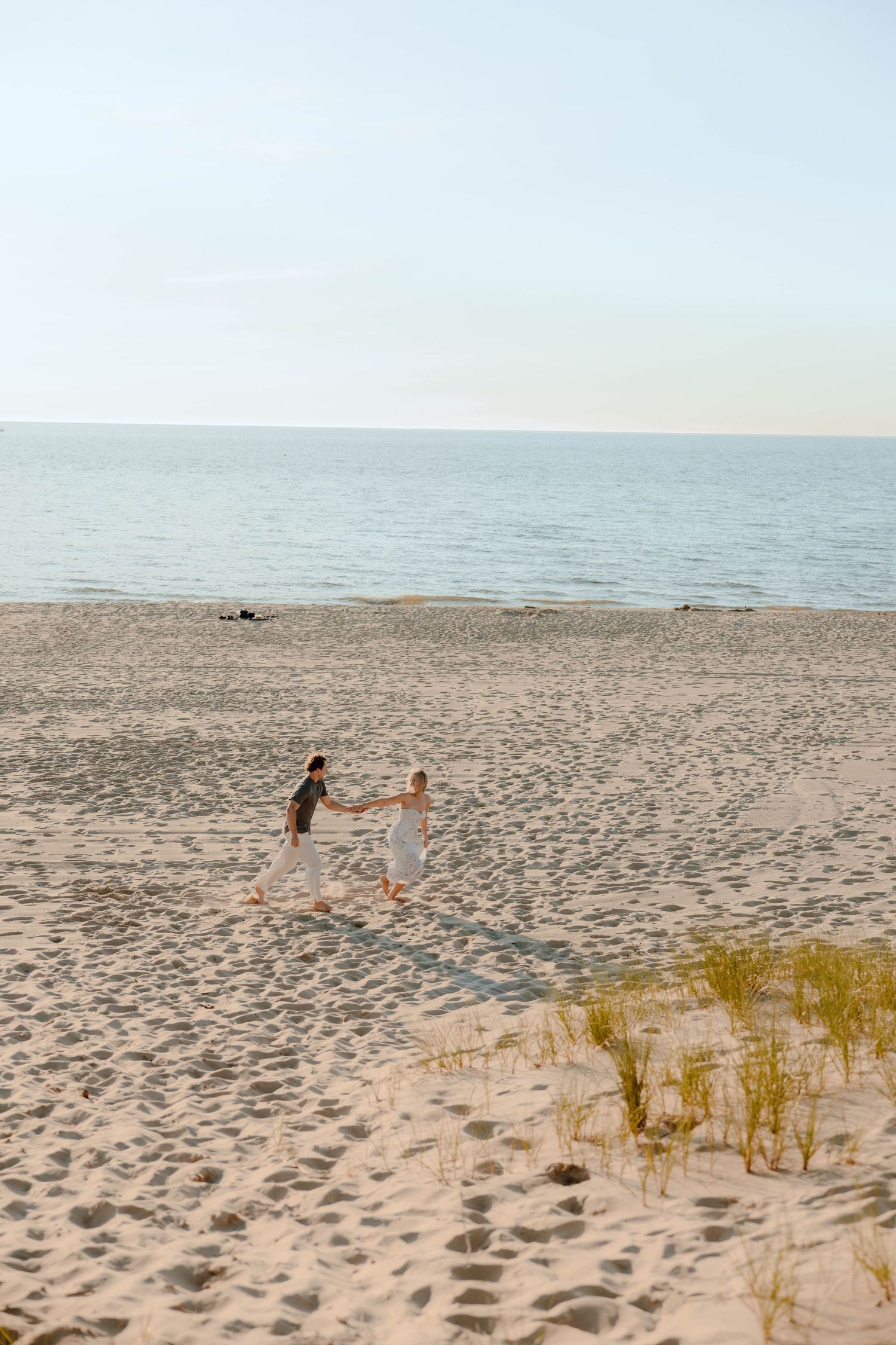 Couple holding hands walking toward the ocean on a sandy beach at sunset.