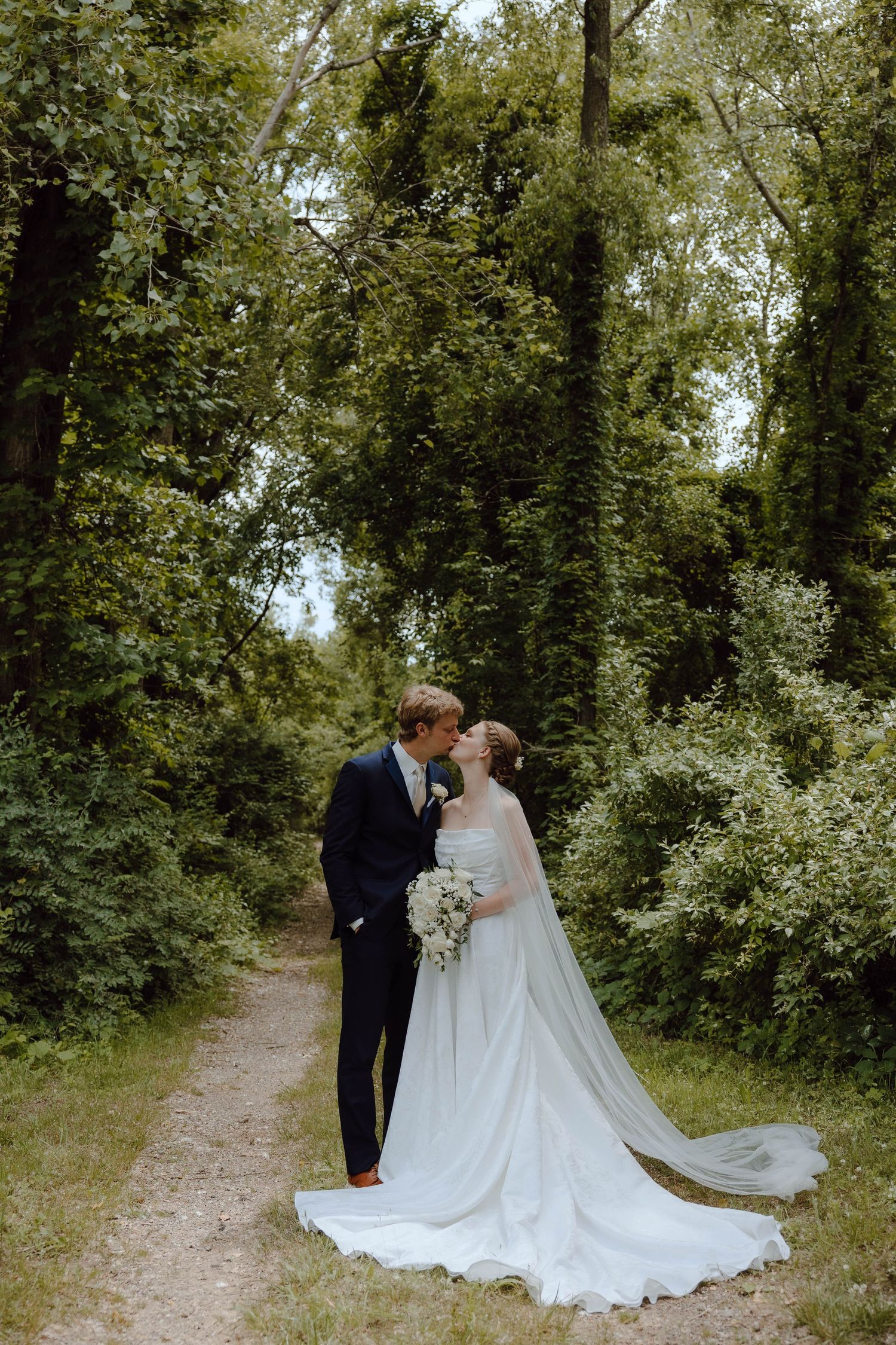 Couple in wedding attire shares intimate moments on a wooded path.