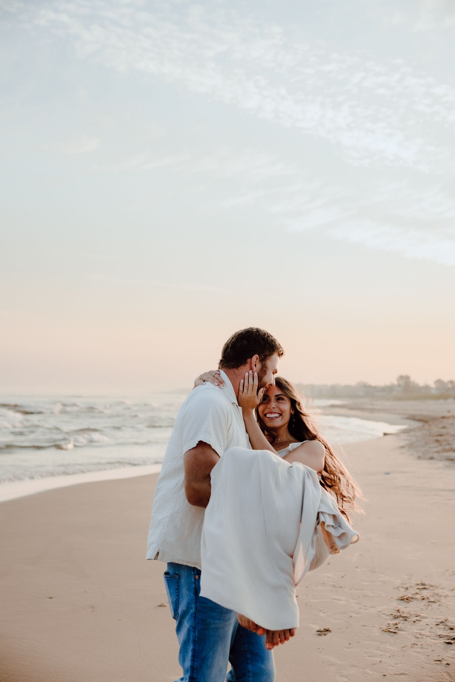 Couple embracing and laughing together on a serene beach at sunset.