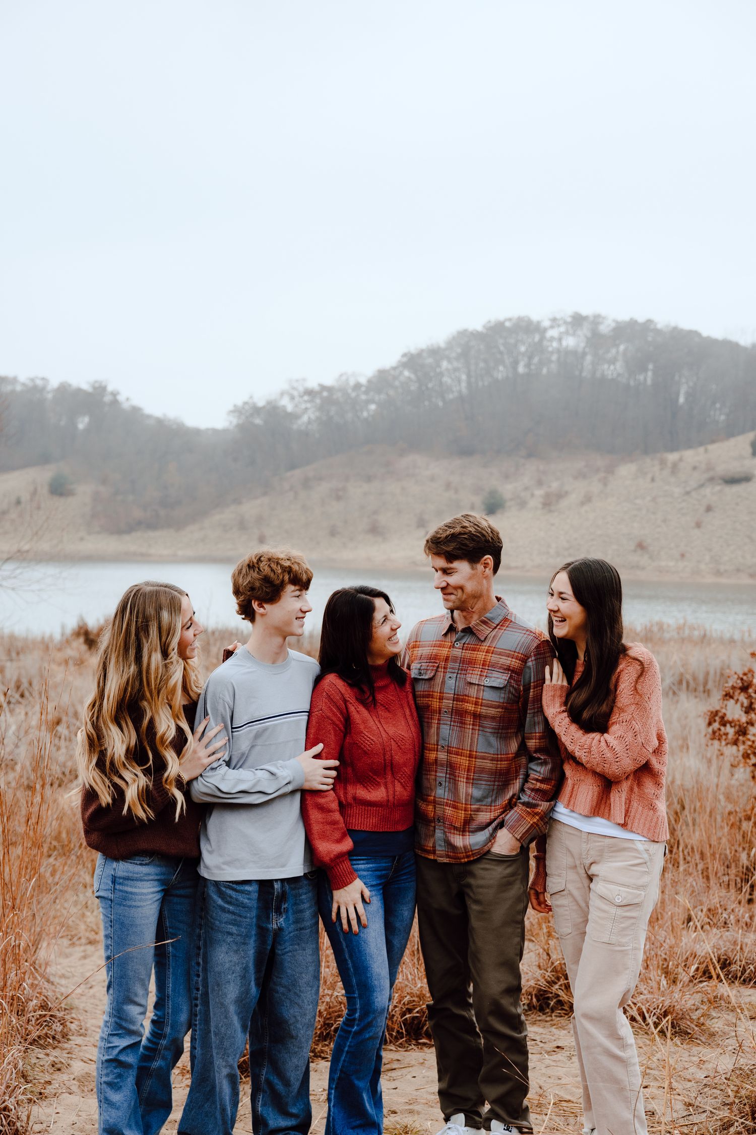 A group of friends pose together on a trail near a lake and wooded hillside.