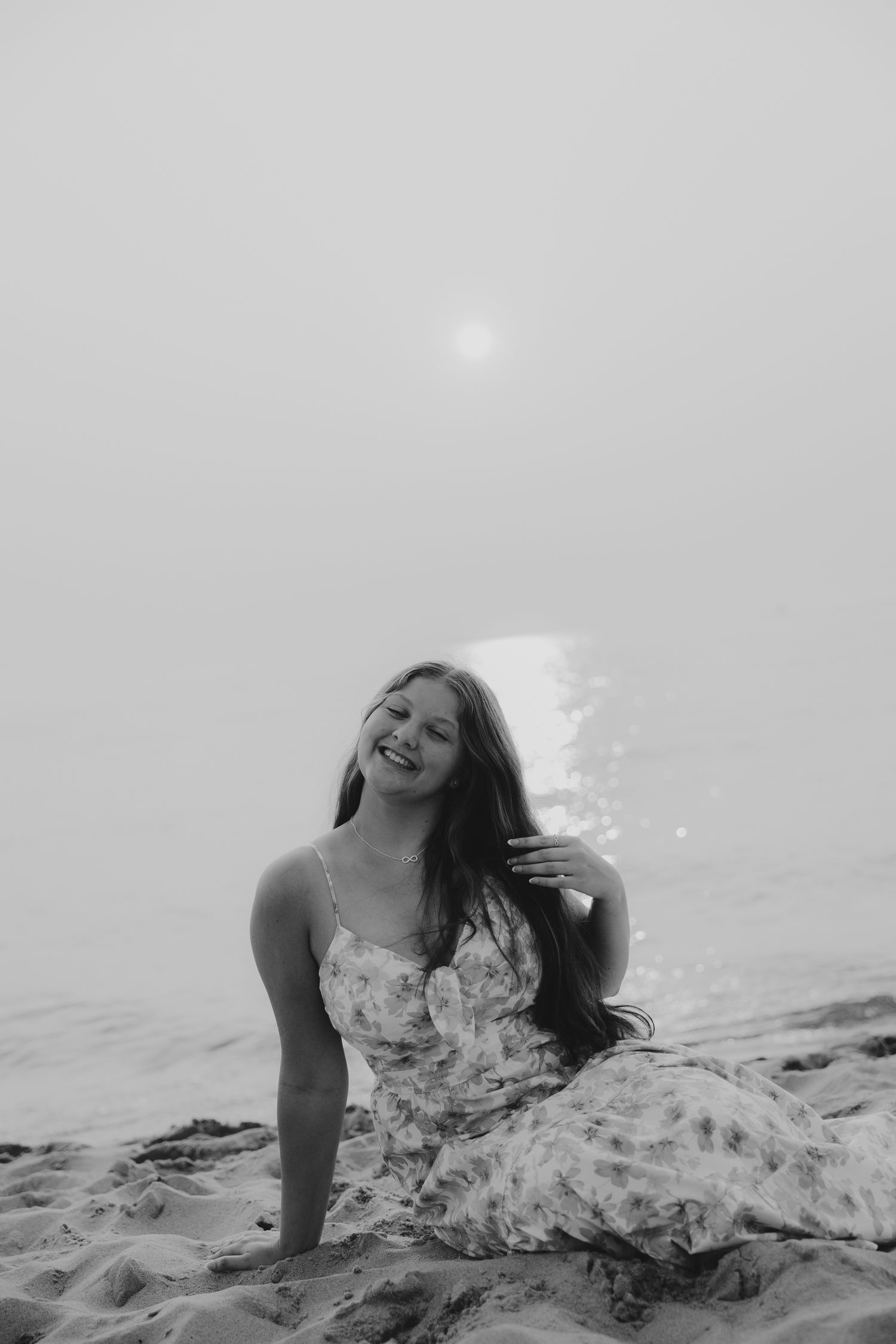 Black and white portrait of person sitting on beach sand with joyful expression.