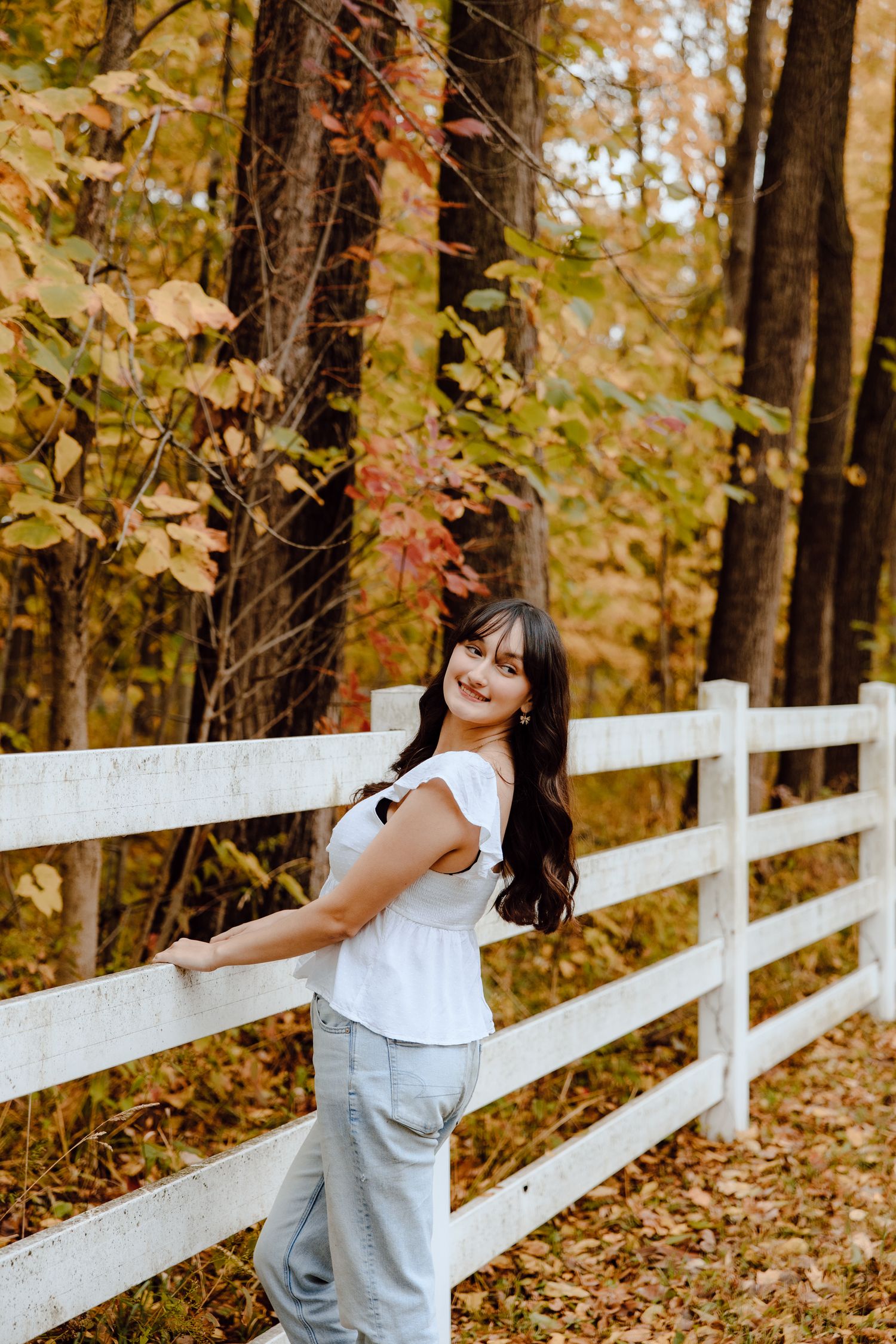 Playful poses along a white fence during an autumn photo session in the woods.