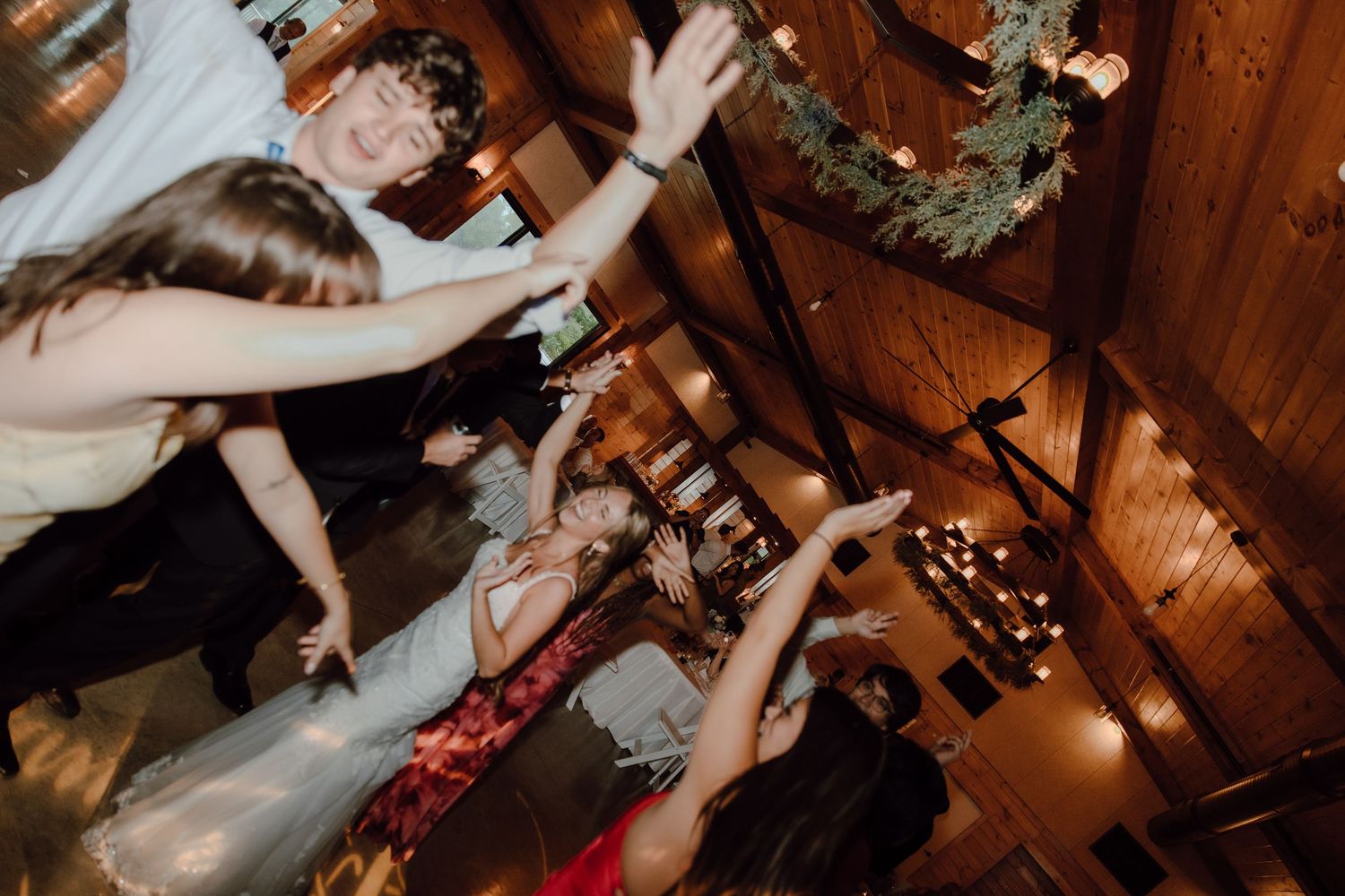 Guests dancing at a wedding reception in a warmly lit rustic wooden venue.