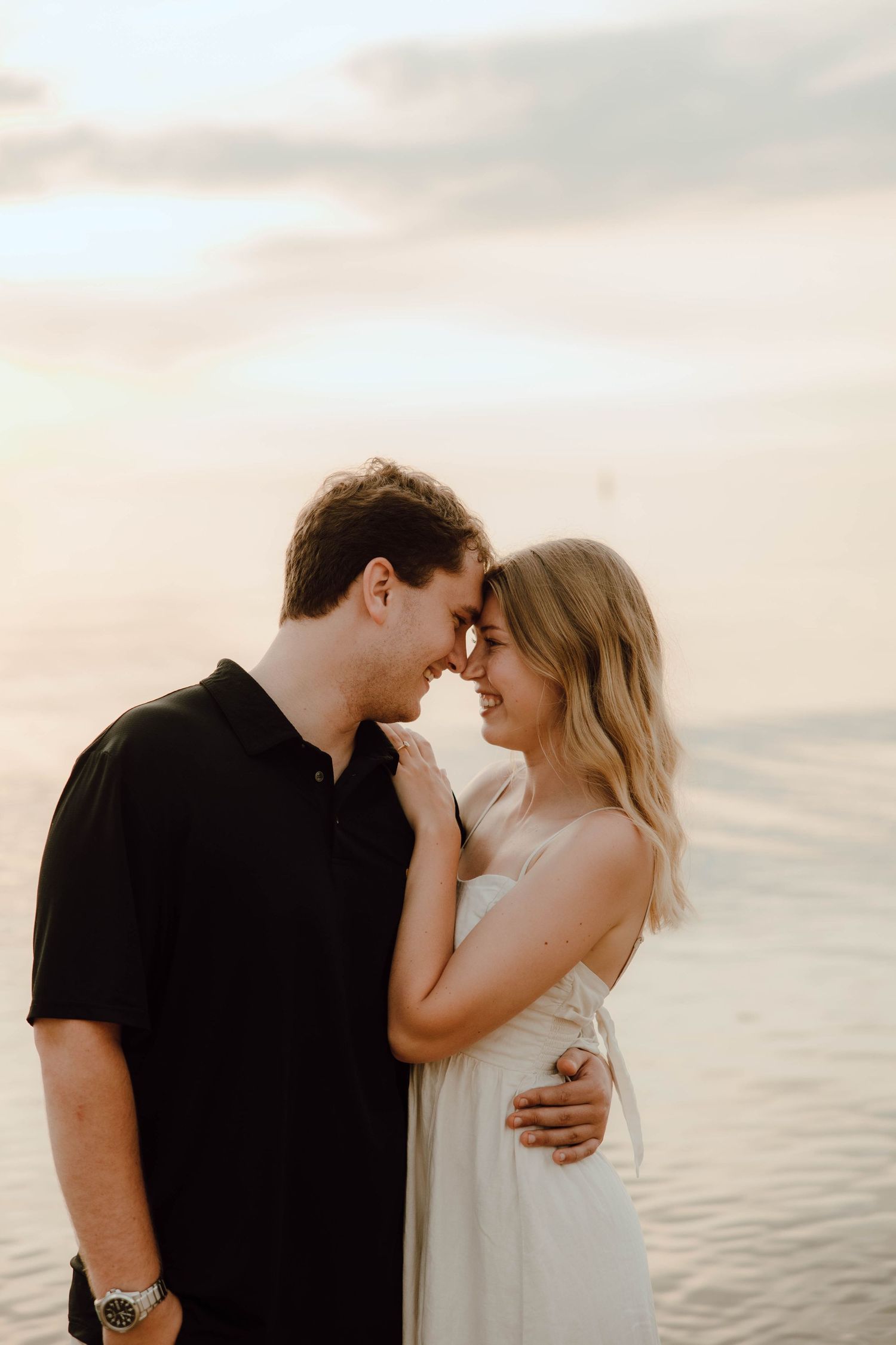 Romantic couple in black and white outfits sharing an intimate moment on a sandy beach at golden sunset.