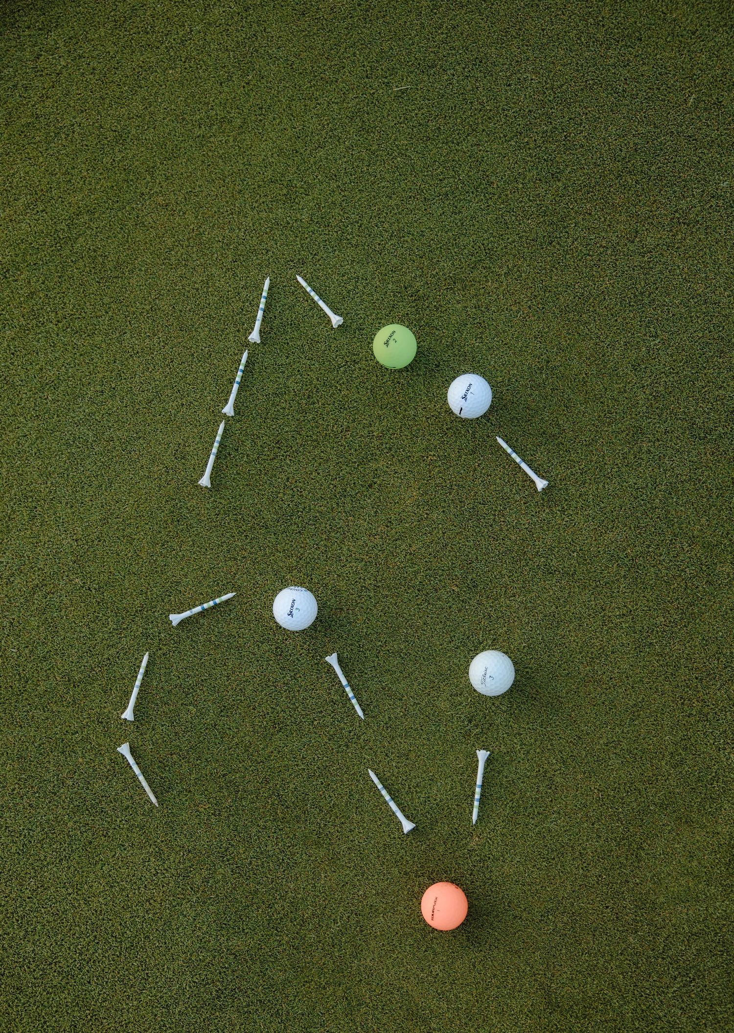 Colorful golf balls and tees arranged on green turf grass in a creative pattern layout.
