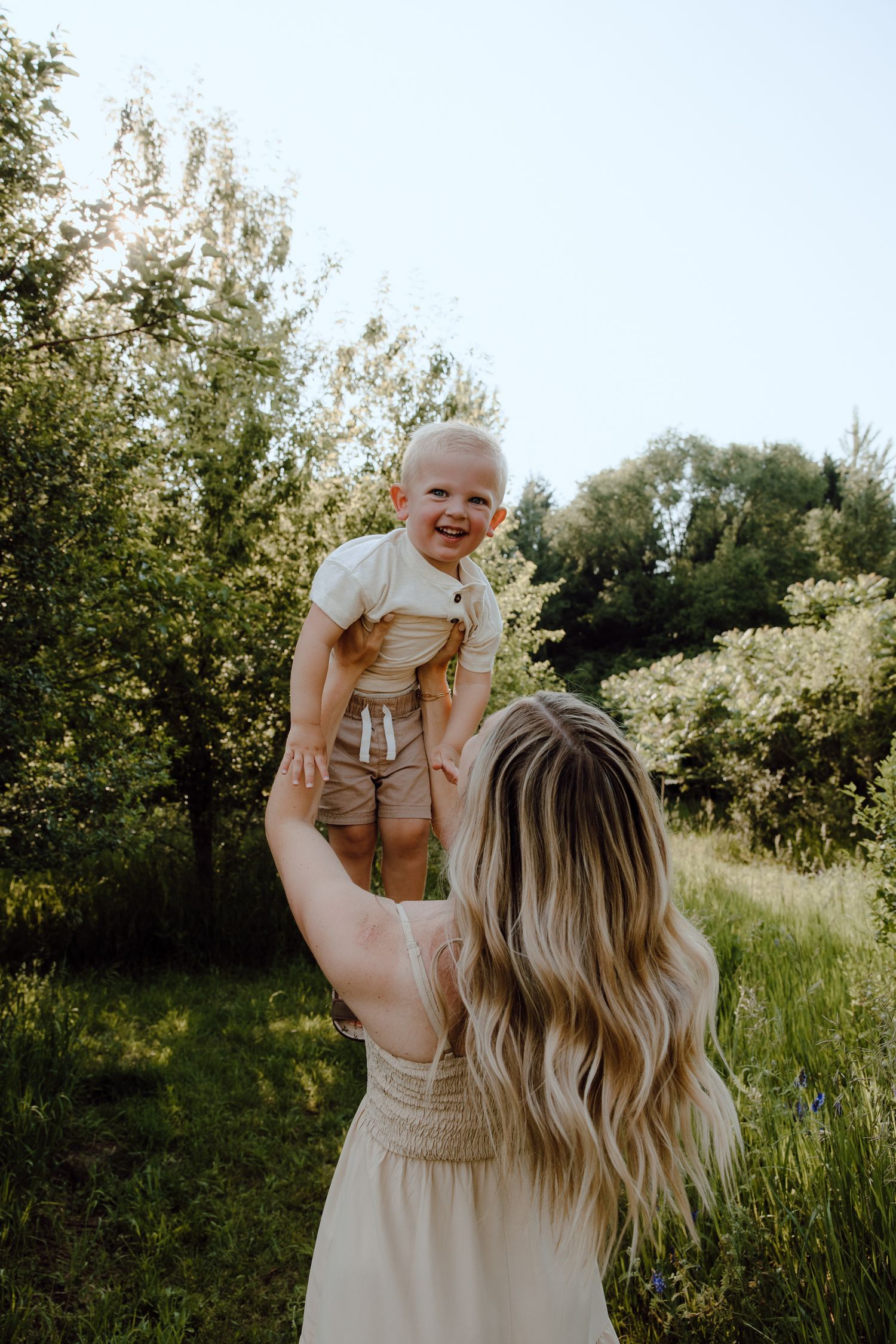 Joyful moment captured as parent lifts child up against natural outdoor backdrop.