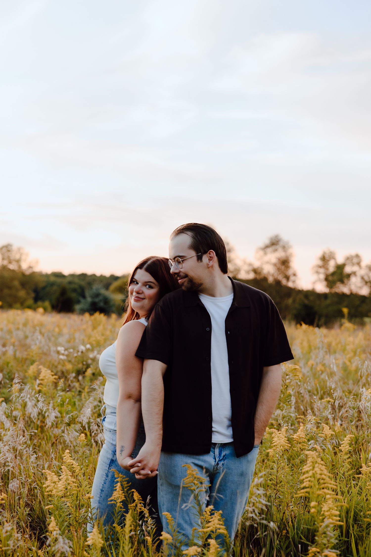 A couple poses together in a golden wildflower meadow during sunset.