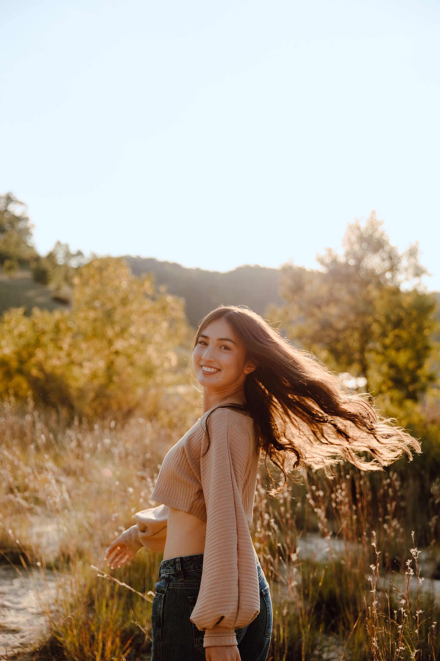 Golden hour portrait session in tall grass with warm sunlight and flowing hair.