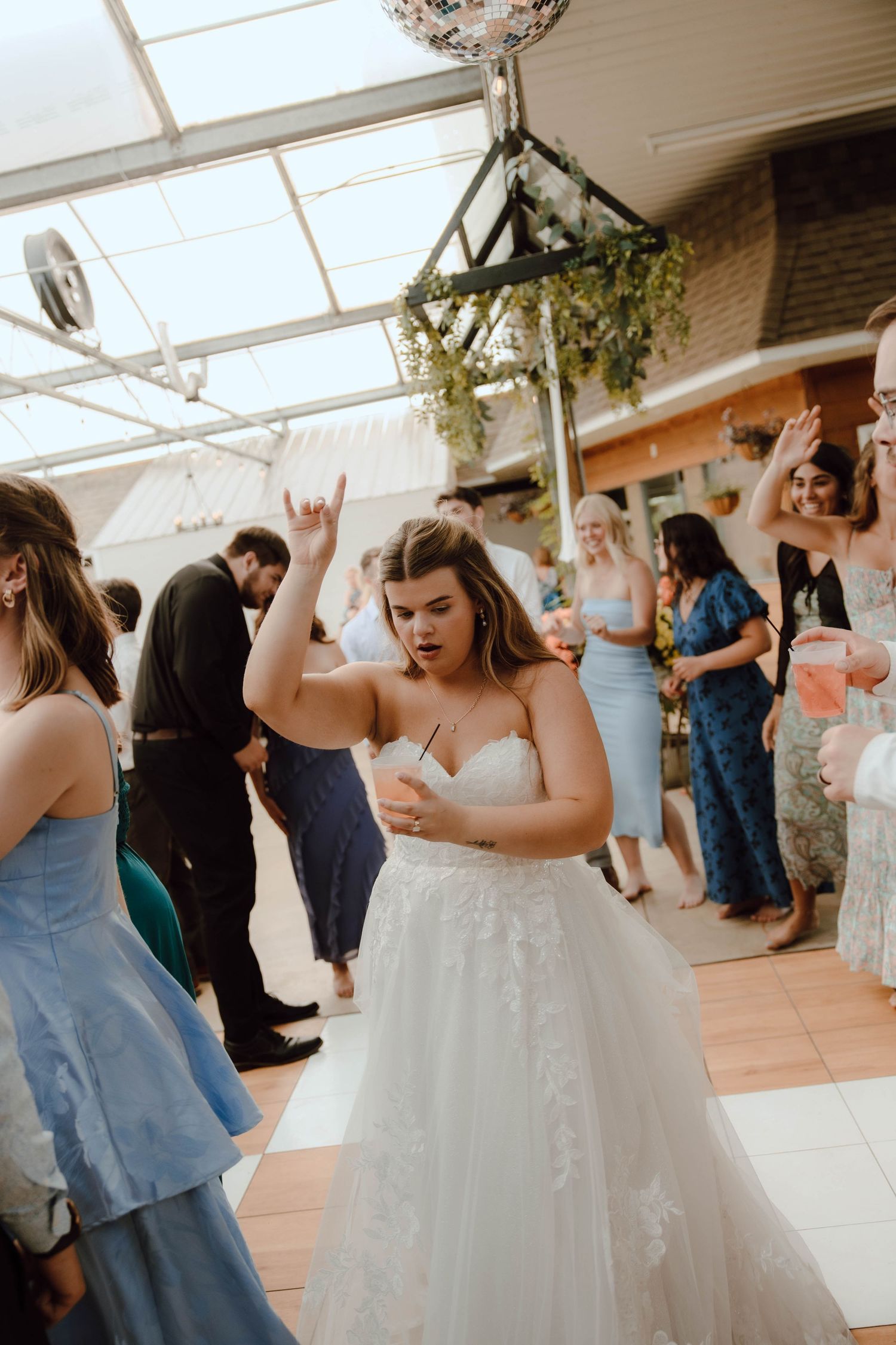 Bride in a strapless lace wedding gown dances joyfully with raised arm at a lively indoor wedding reception.