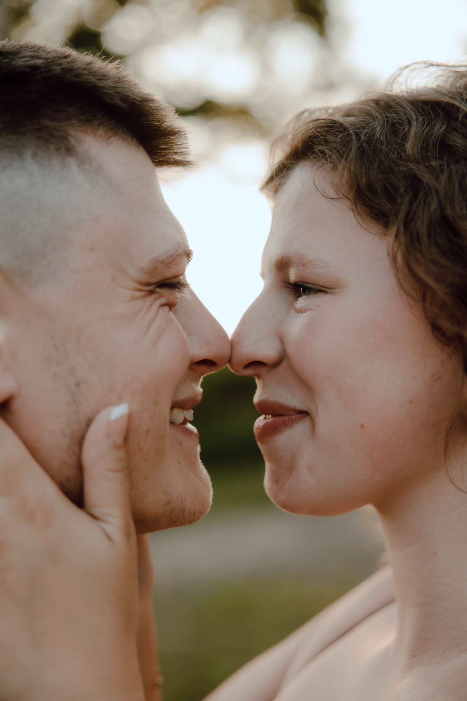 A couple smiling and touching noses in a tender romantic moment outdoors with soft natural light.