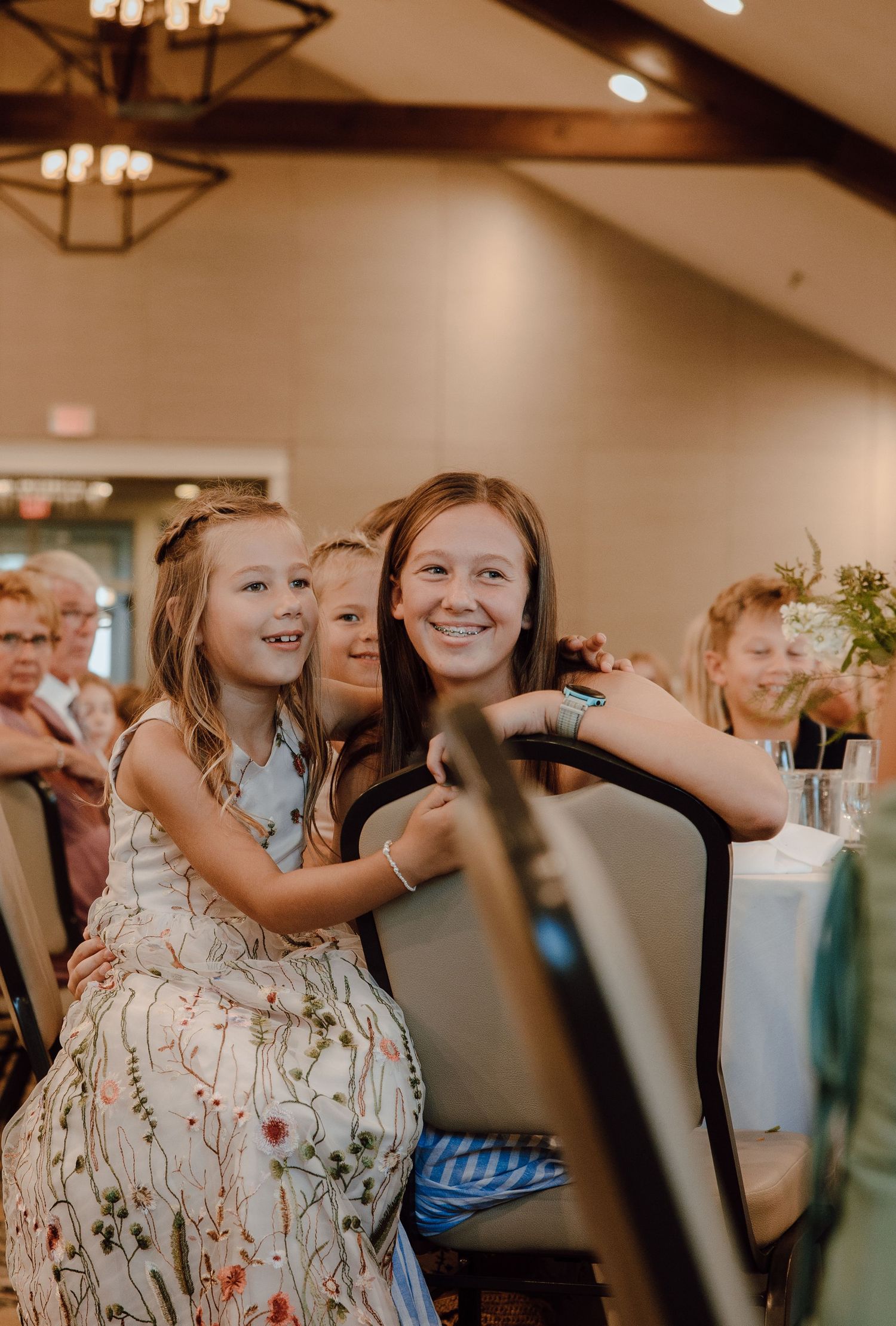 Two young girls smiling and posing together at an elegant indoor wedding reception venue.