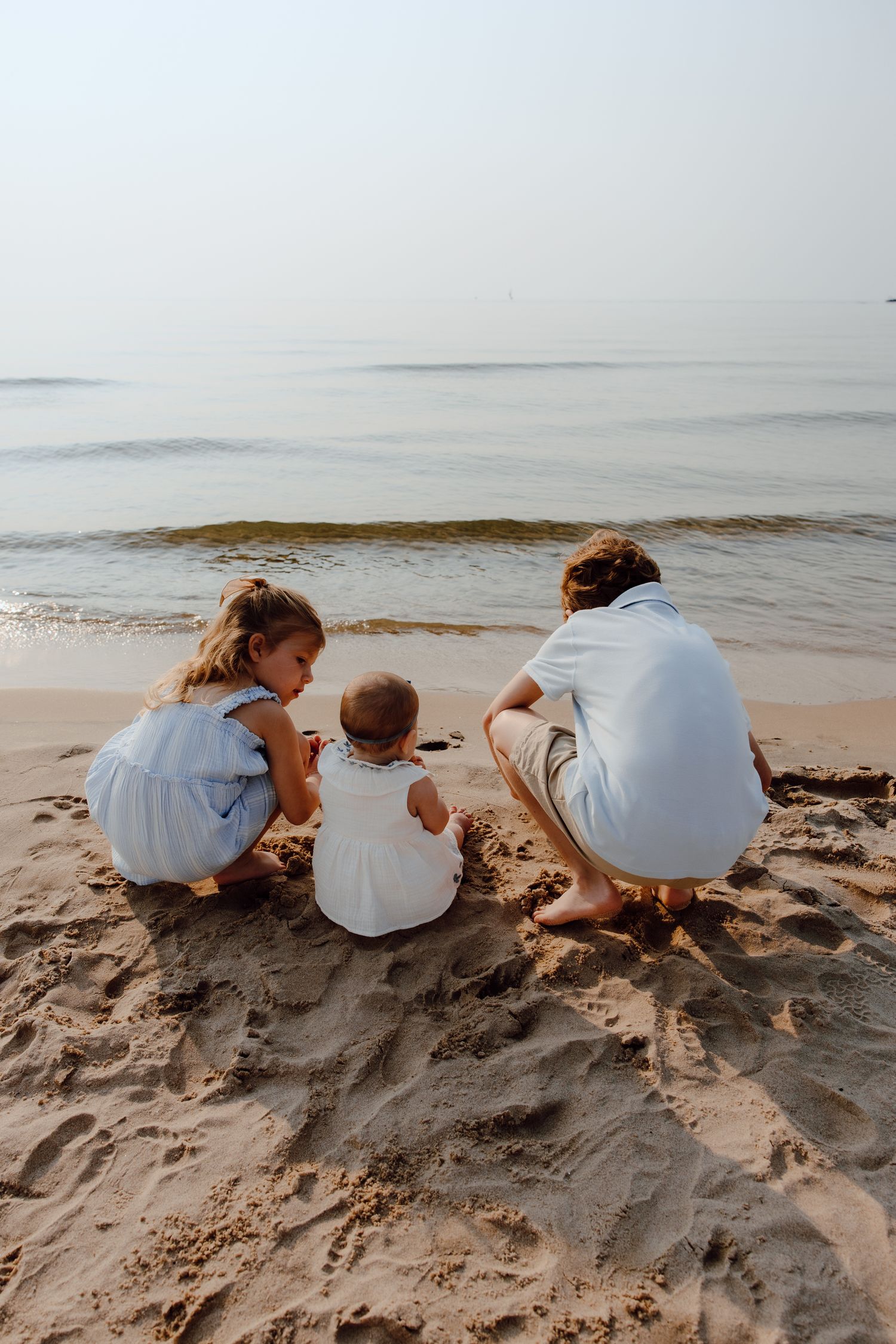 Family in white shirts explores and plays together on a sandy beach.
