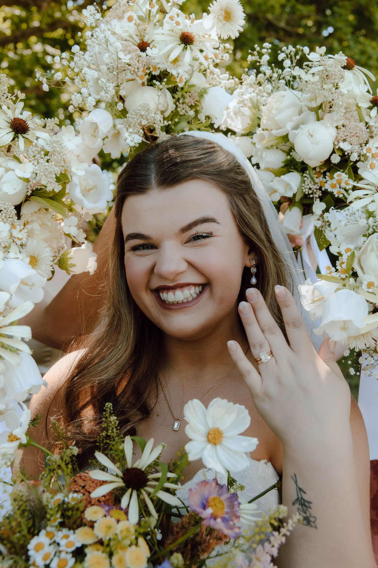 Smiling bride showing off engagement ring surrounded by white wedding flowers.