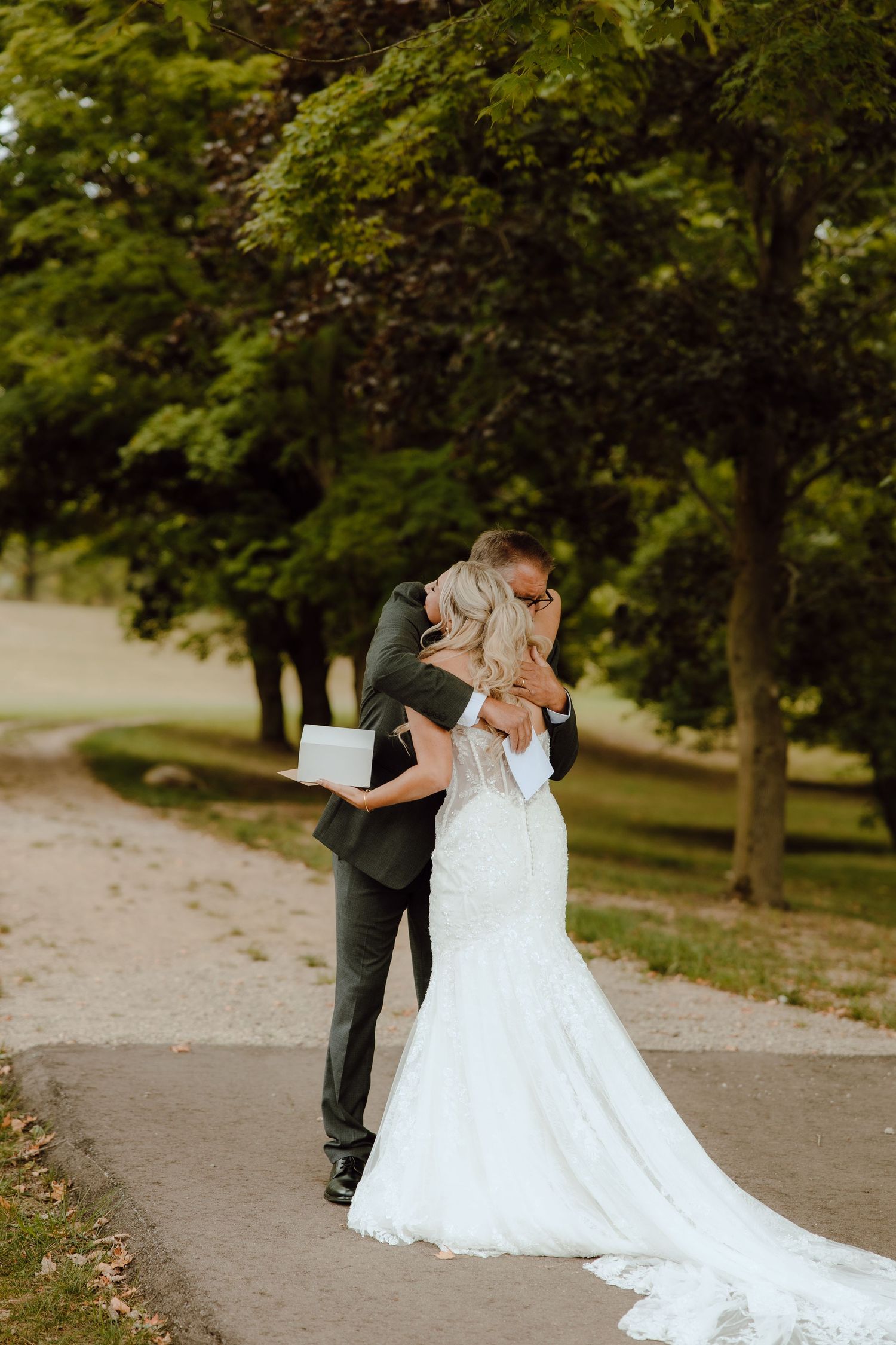 Bride and groom sharing an emotional first look embrace on a garden path, wearing white mermaid gown and dark suit.