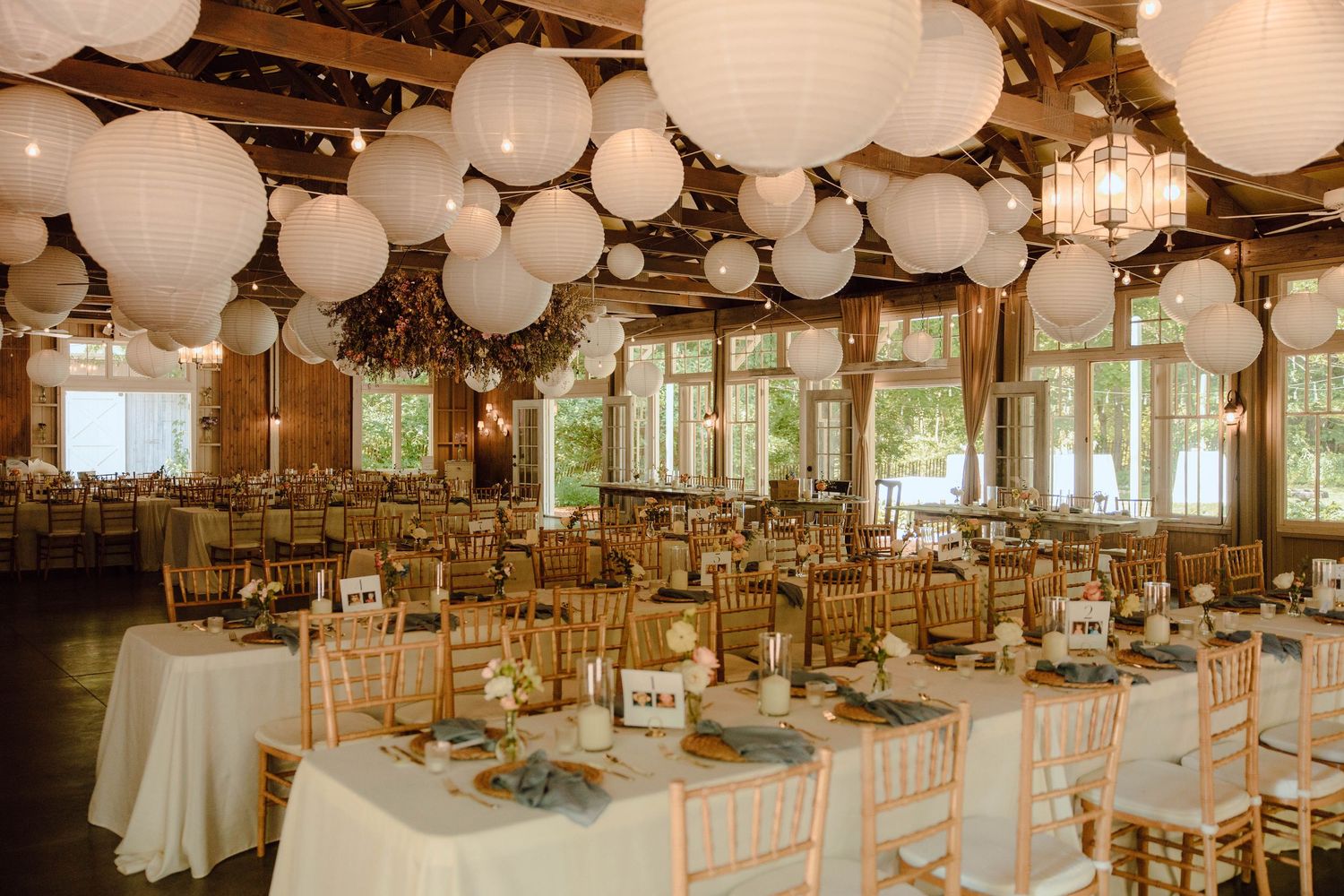 Elegant wedding reception hall with white paper lantern ceiling decor, gold chiavari chairs, and white linen tablecloths.