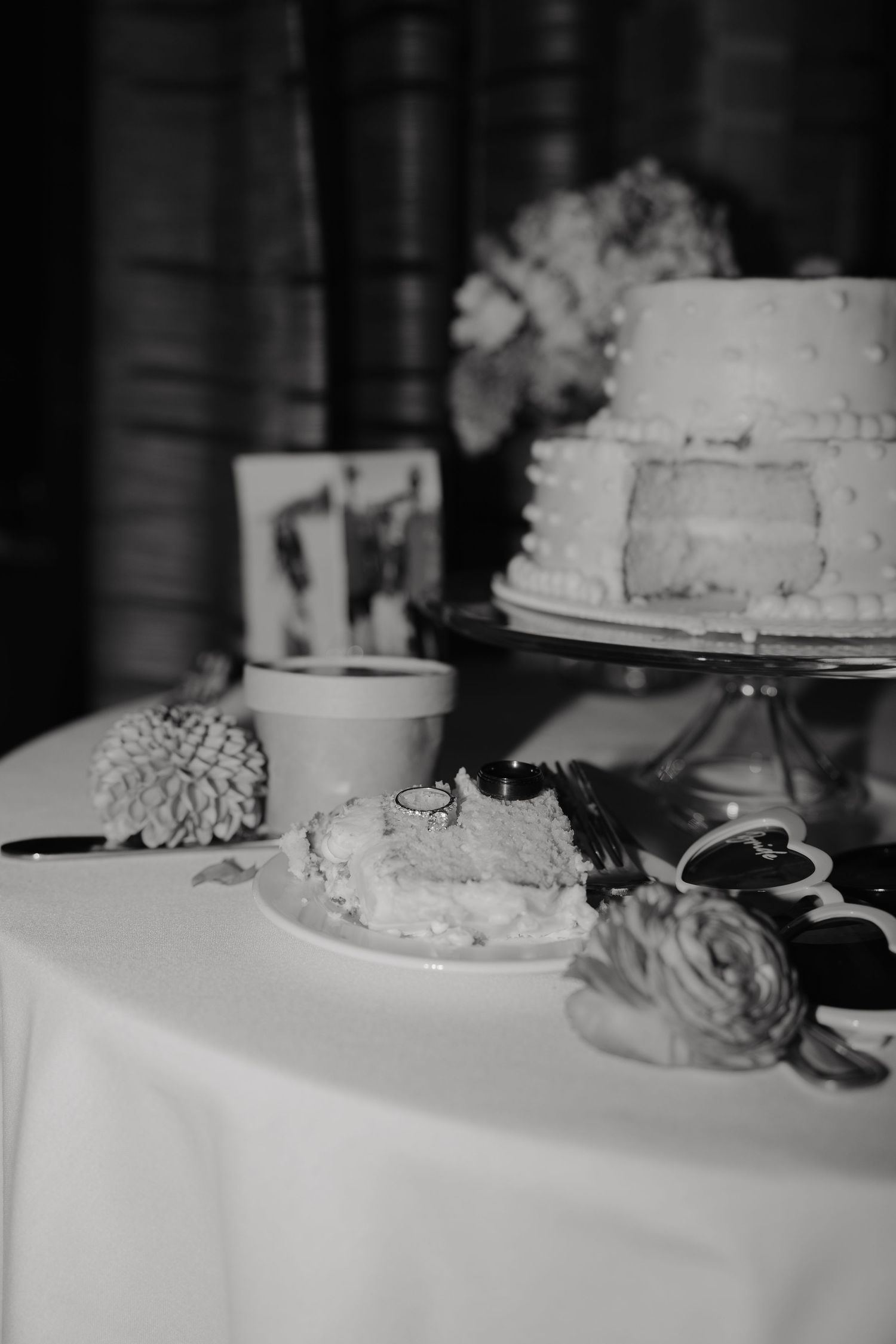 Elegant two-tier wedding cake with a slice and rings on a white tablecloth in black and white.