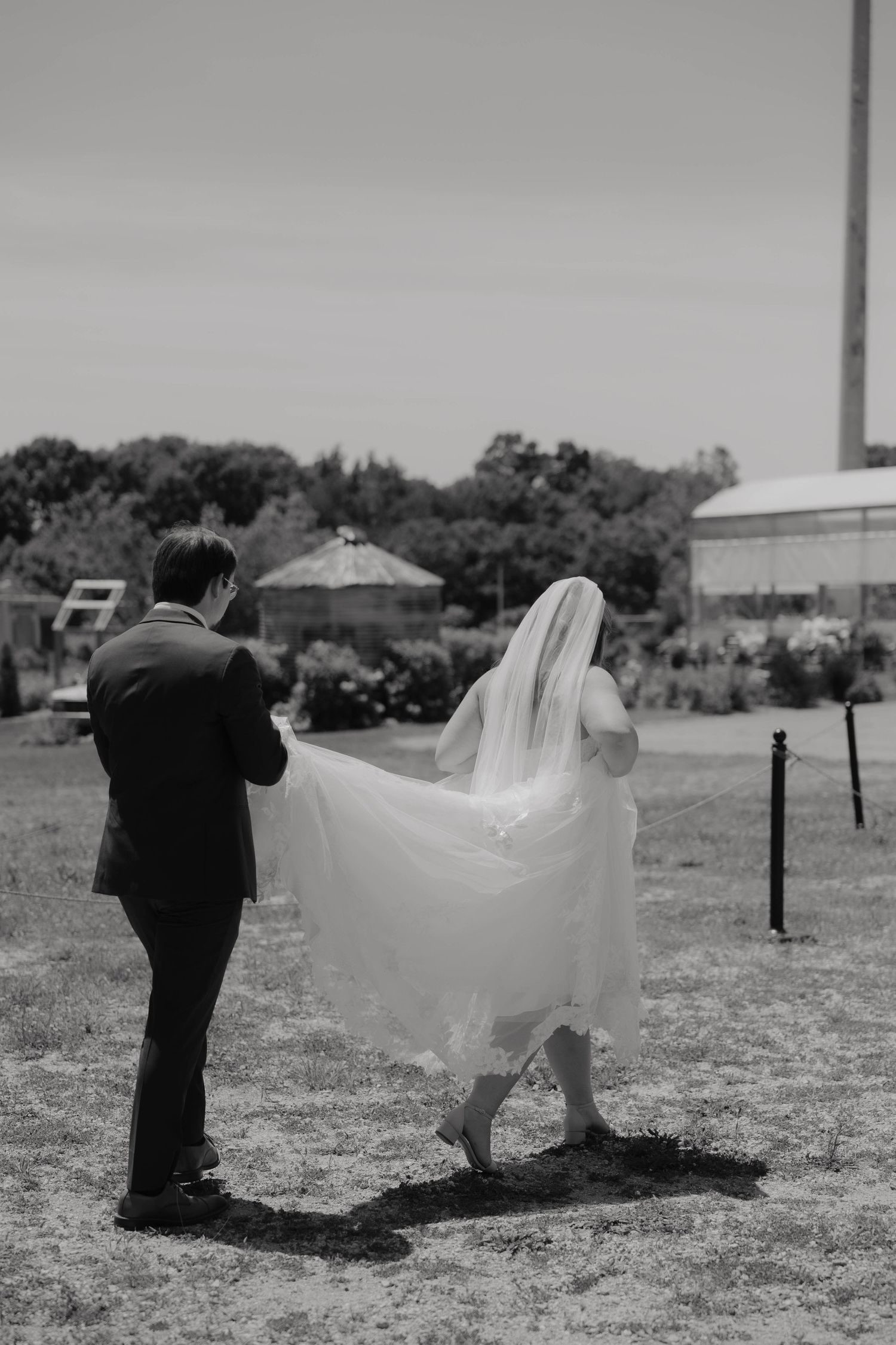 Black and white photo of a groom lifting his brides veil outdoors on their wedding day.