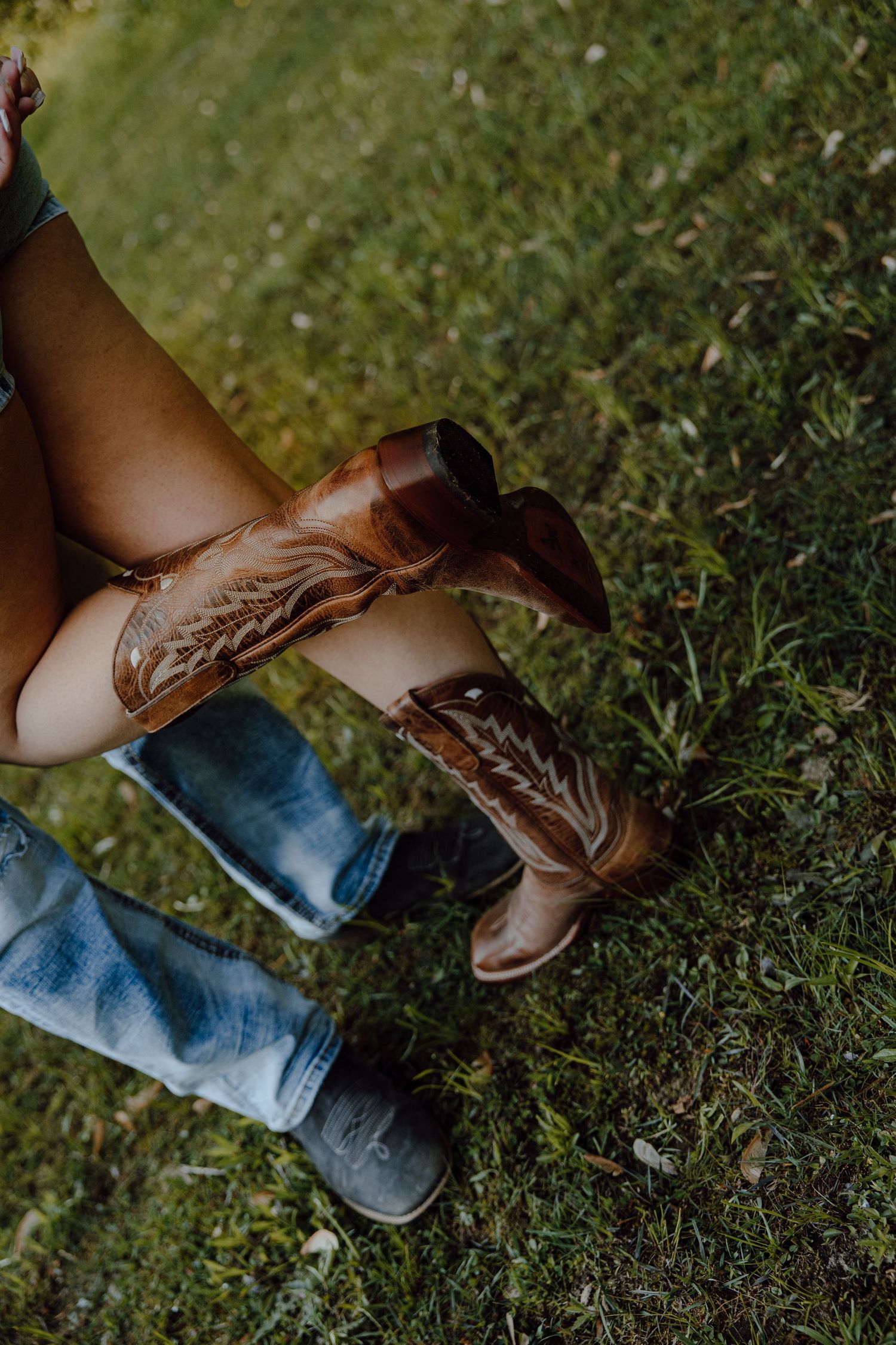 Detail shot of brown cowboy boots on grass with denim jeans.