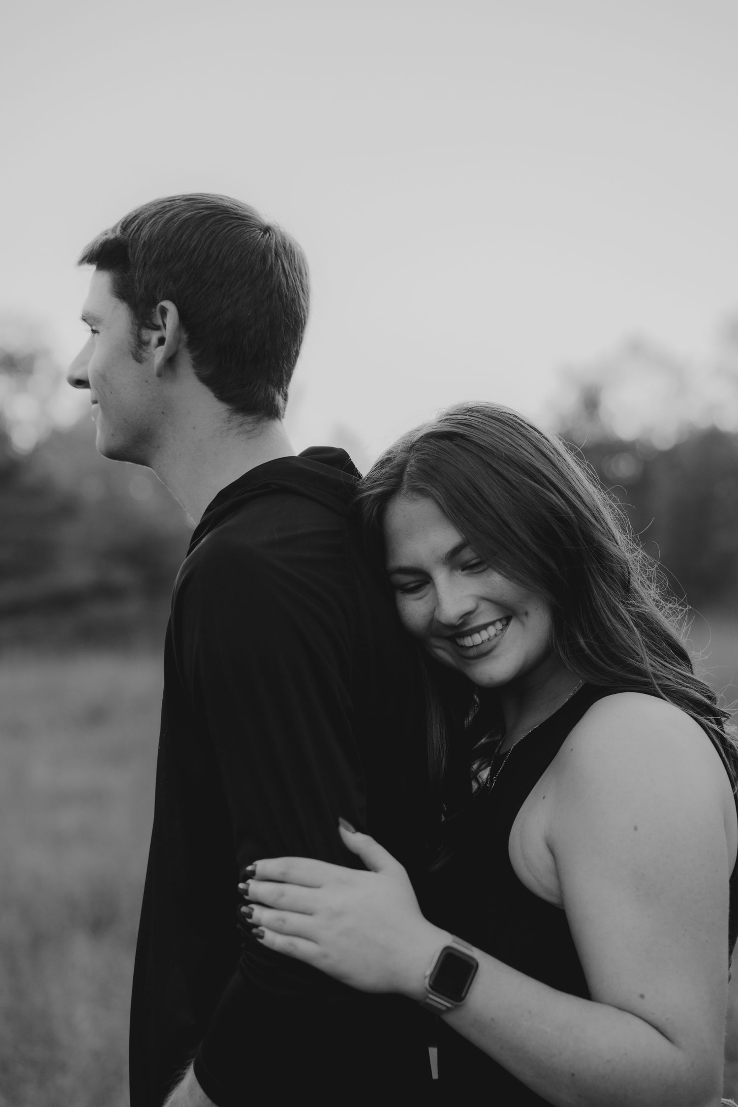 Black and white photo of couple embracing outdoors with joyful expressions.
