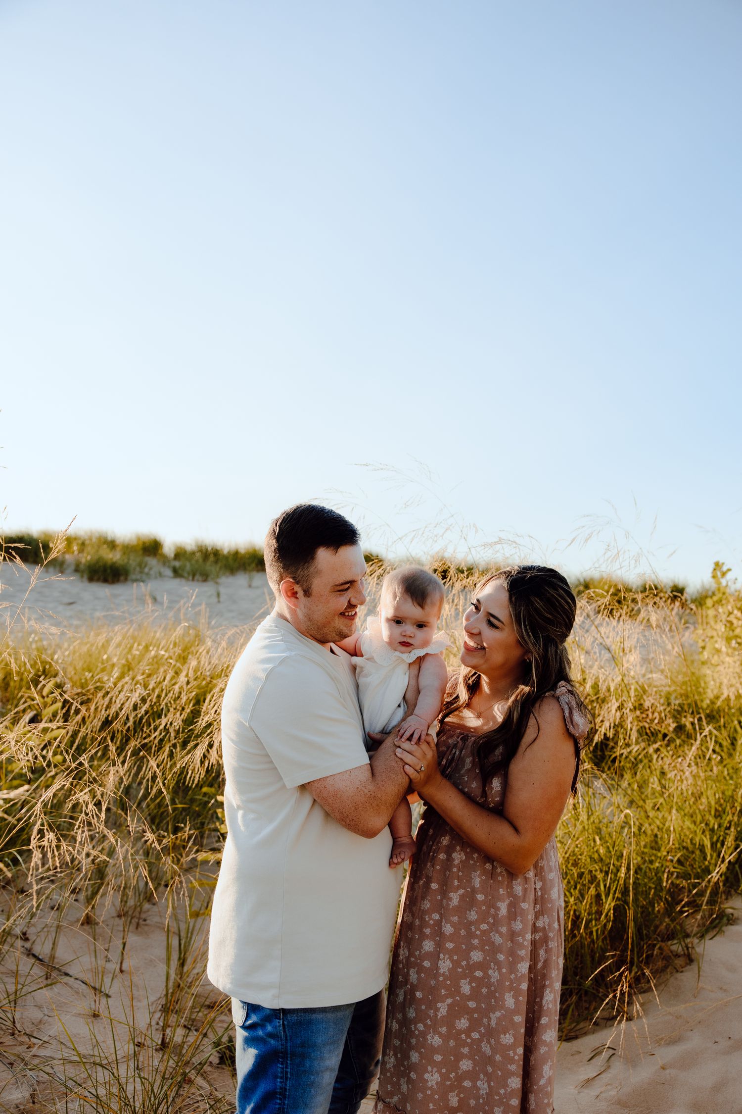 A joyful family moment captured against a sunny beach backdrop with tall grass.